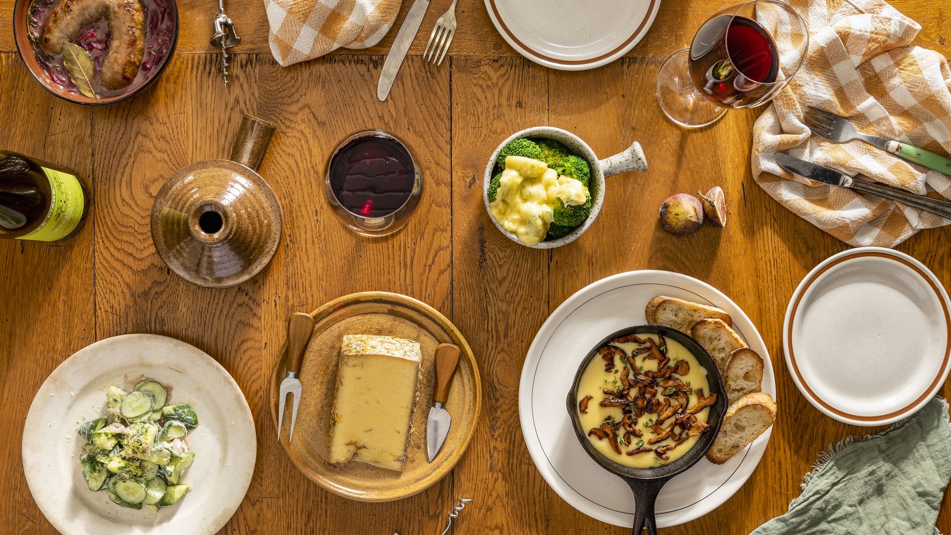 An array of food is set out on a wooden table, including cheese and wine and crusty bread.