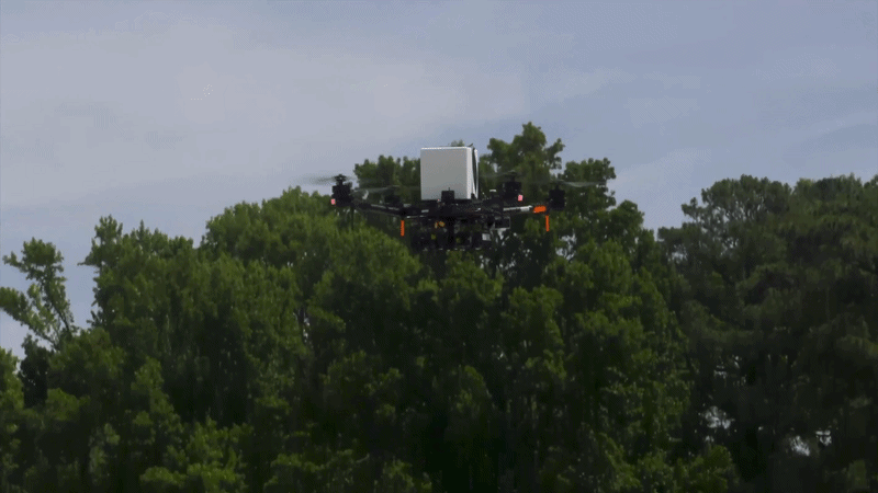 a video of a drone carrying a white box and landing