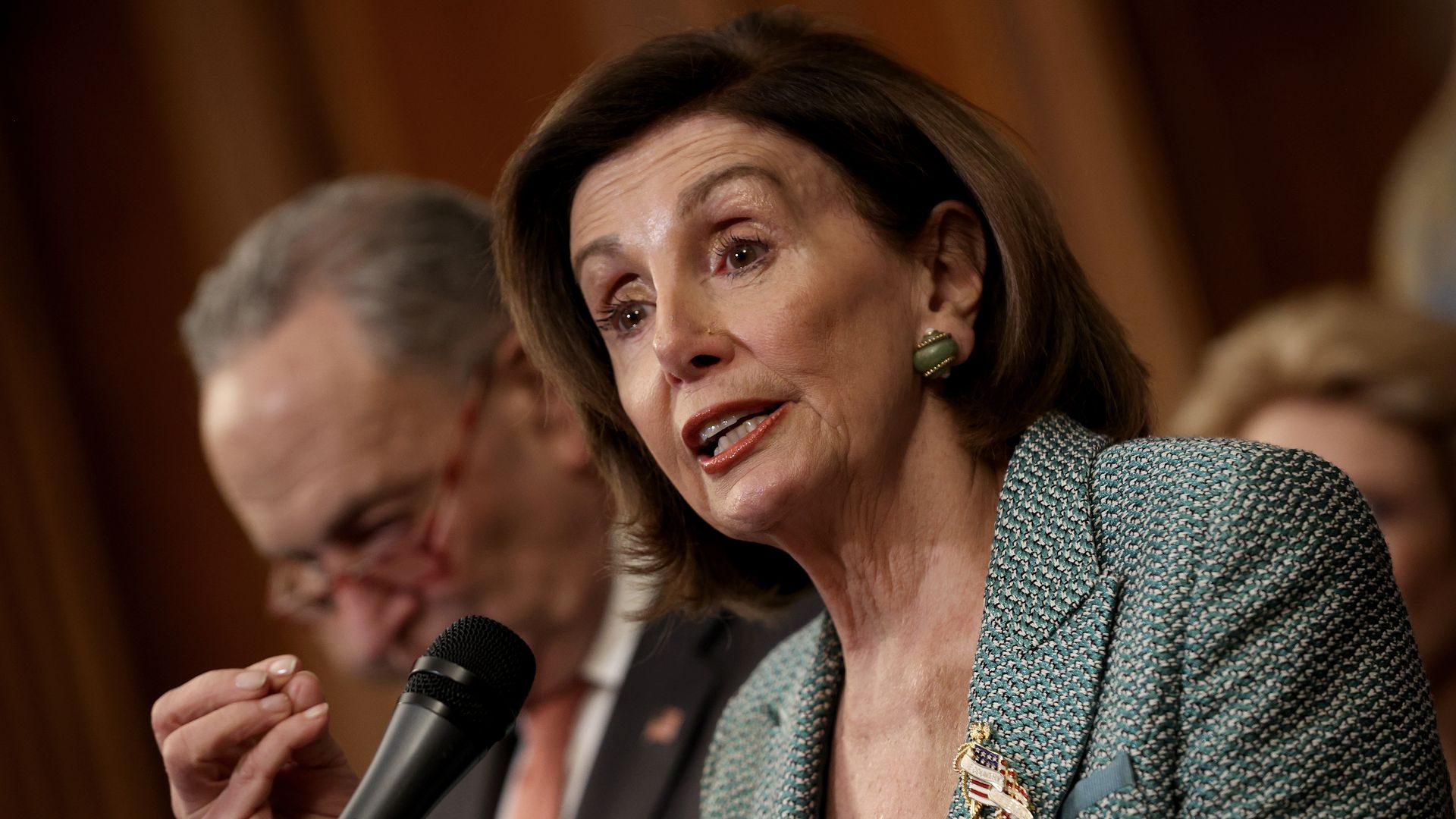 Nancy Pelosi speaking with Chuck Schumer behind her