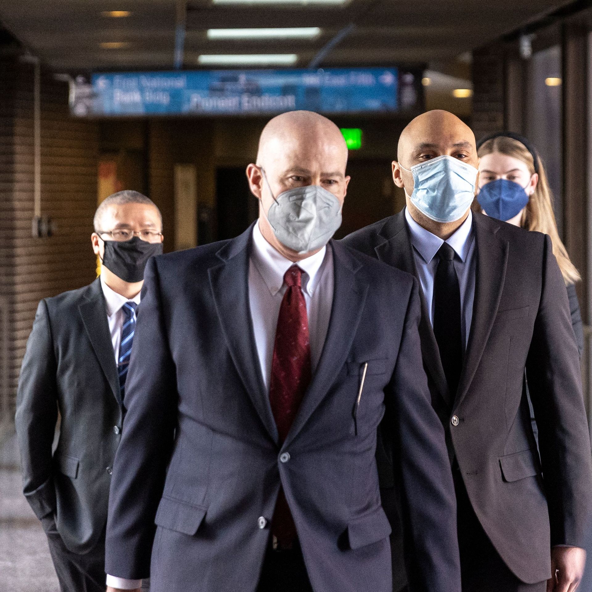 Photo of three masked men and a masked woman in the back walking down a hallway
