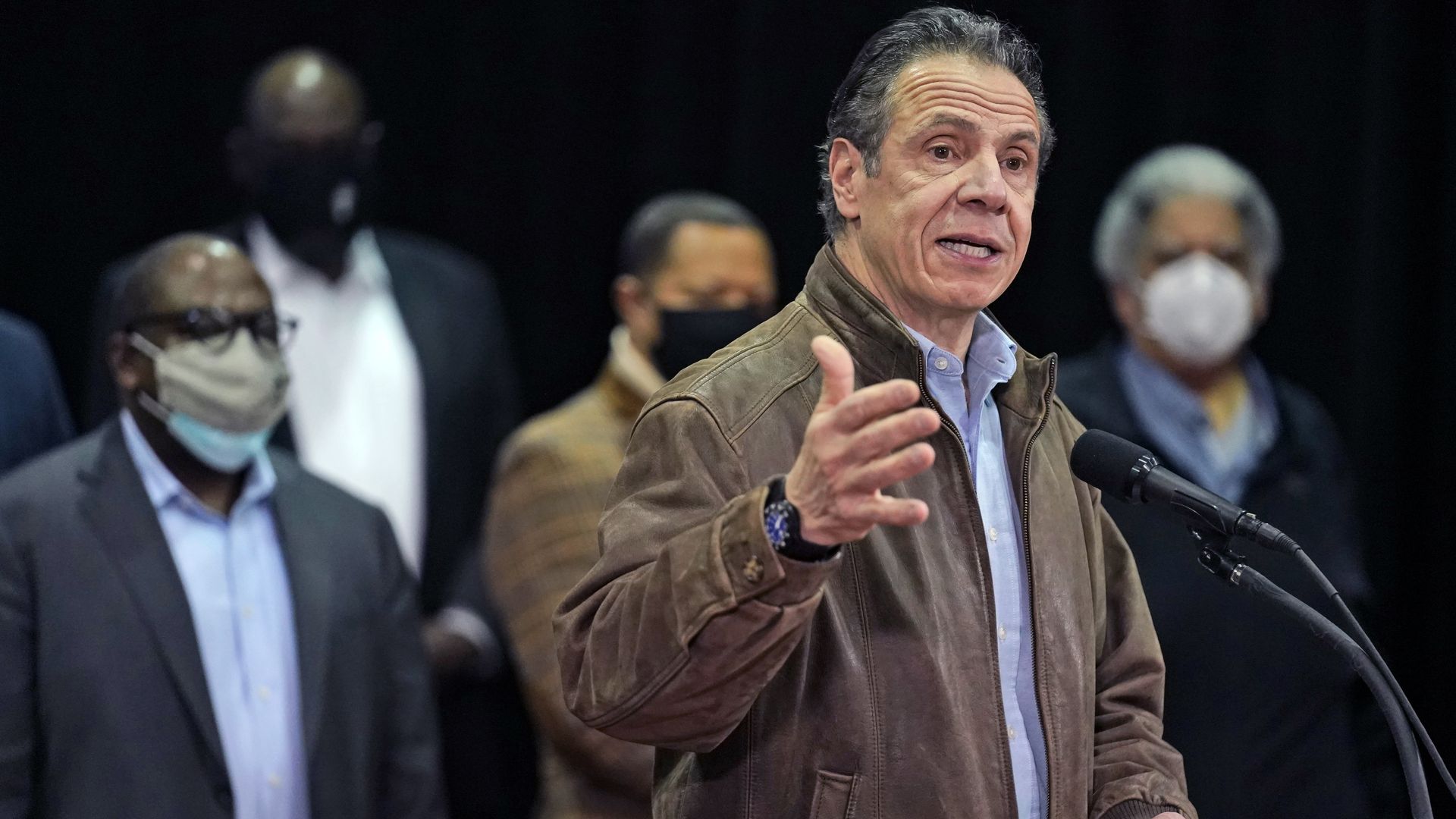 Andrew Cuomo wears a jacket and speaks in front of a microphone