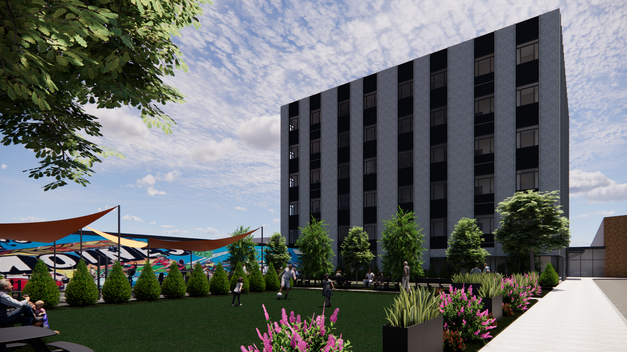 Urban courtyard with a tall dark gray building on the right, a green lawn, trees, and pink flowering planters. A colorful mural wall with orange shade sails; people walk and sit under a blue sky.