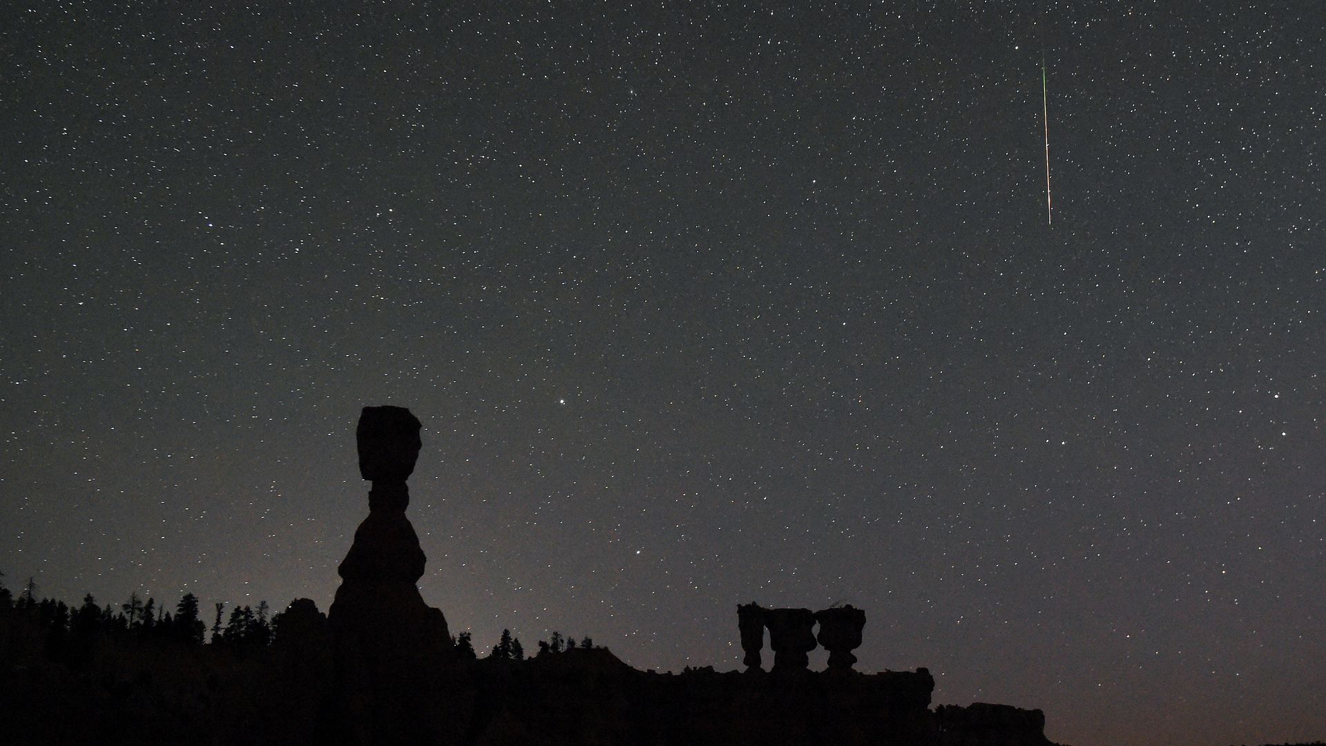 A shooting star falls over hoodoos at Bryce Canyon