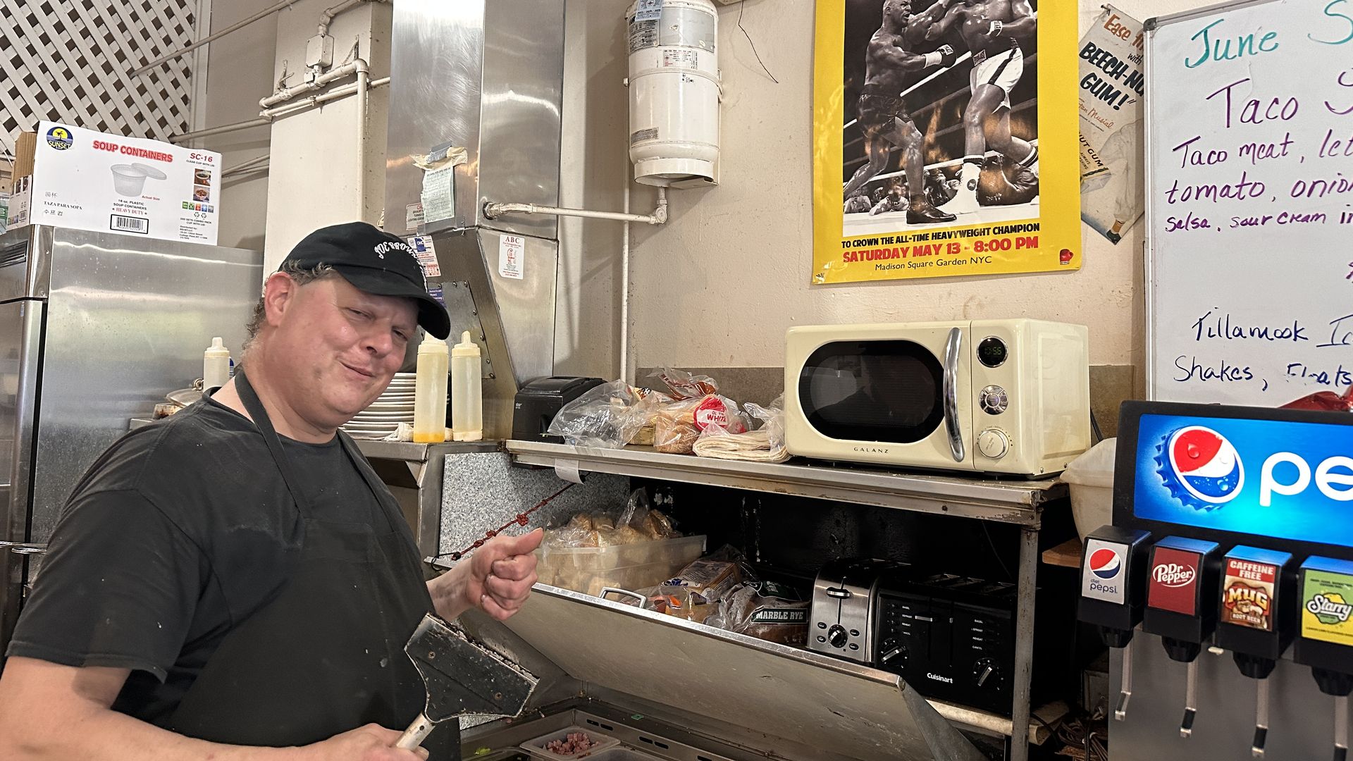 Man with hat and grill scraper in a diner kitchen