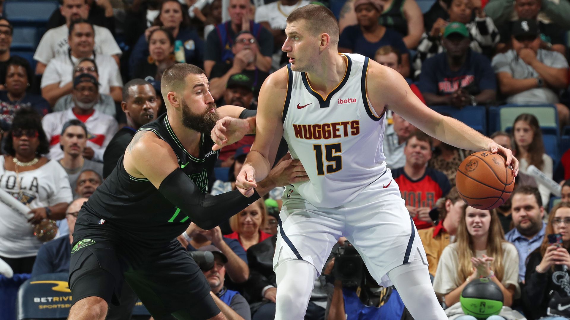 Two men play basketball, with one holding a basketball and another playing defense. 