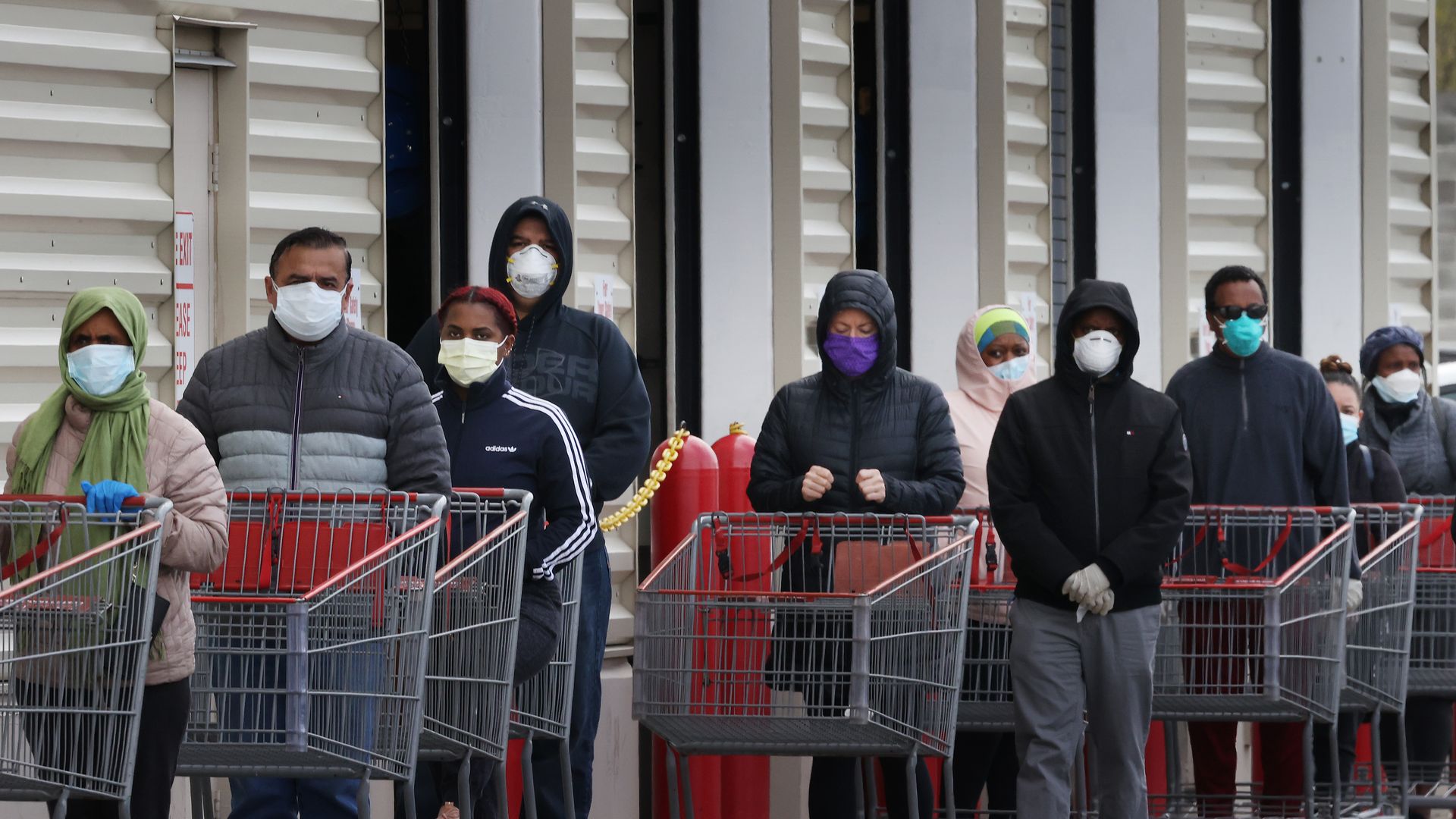 Customers with shopping carts wear face masks while in line to enter a grocery store