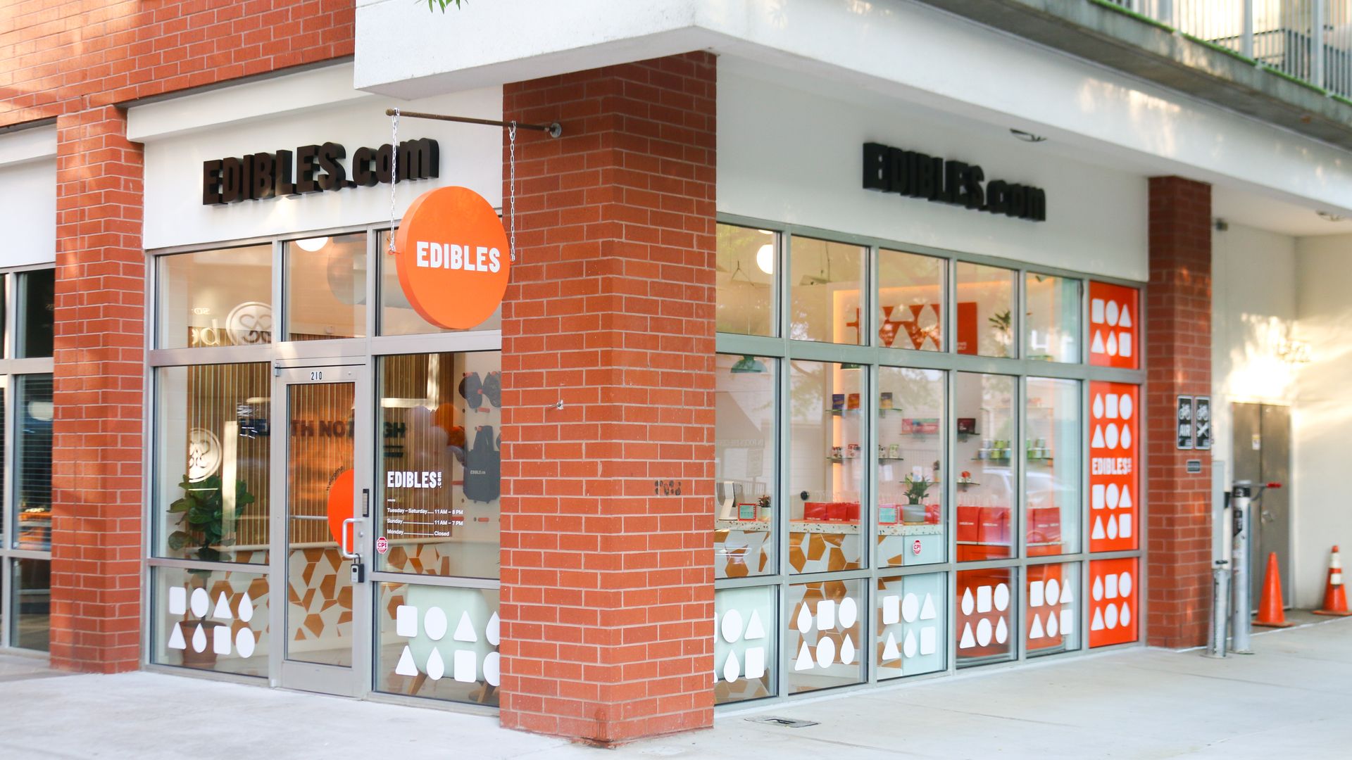 Corner storefront with red brick exterior and large glass windows; a sign reads "EDIBLES.COM" above, and an orange circular sign that says "EDIBLES" hangs over the entrance.