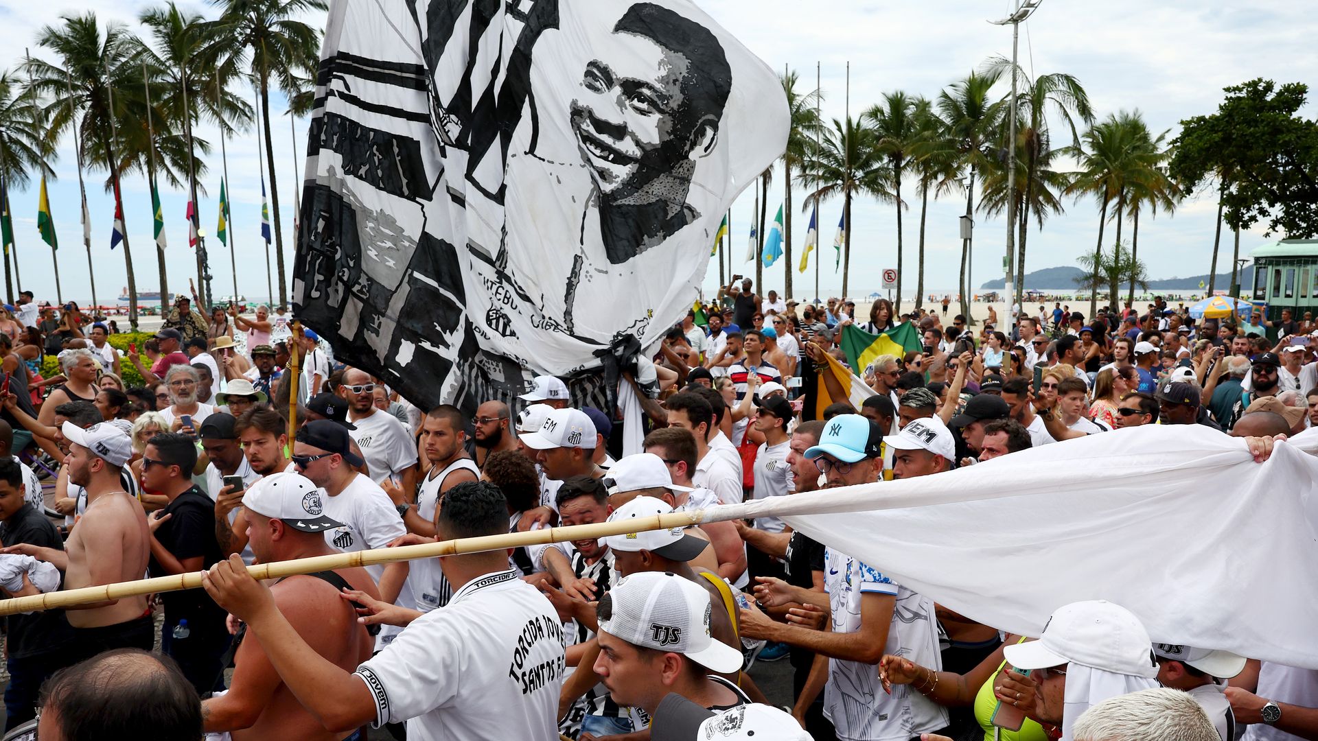 A large crowd of people carry a large banner with Pelé's face on it during his funeral procession