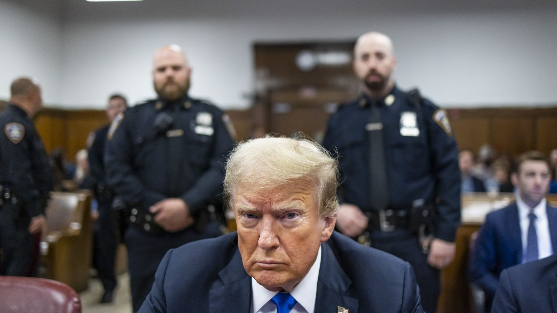 Former President Donald Trump sits at the defendant's table inside a Manhattan courthouse flanked by police officers.