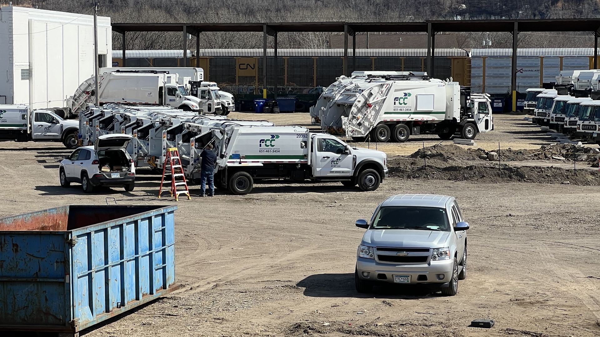 White waste pickup trucks with the "FCC Environmental" logo on the side sitting on a dirt lot