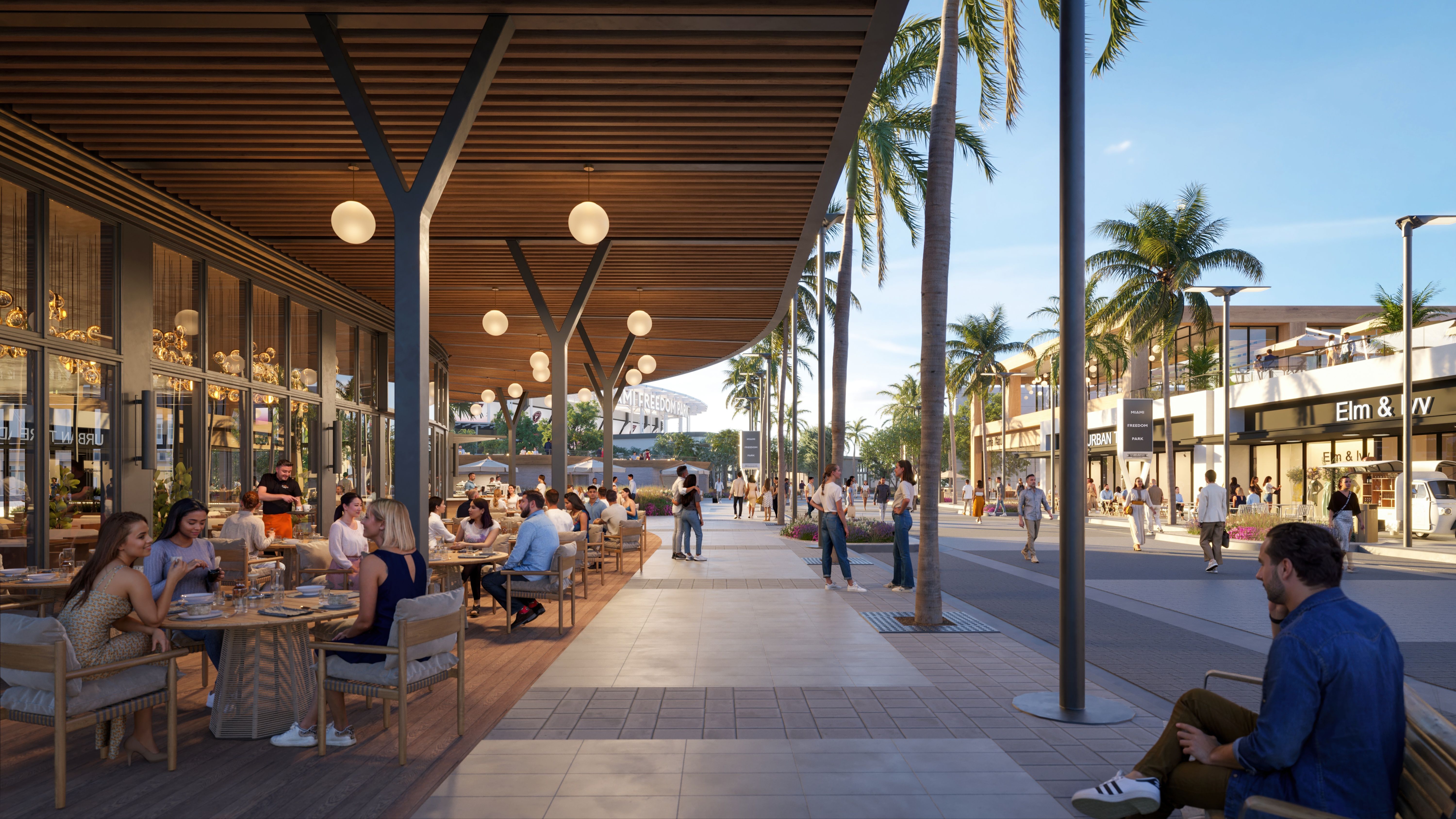 A rendering of Miami Freedom Park showing an outdoor dining area on a sunny day with people sitting at tables under a wooden canopy, palm trees lining the walkway, and shops in the background. A man sits on a bench nearby.
