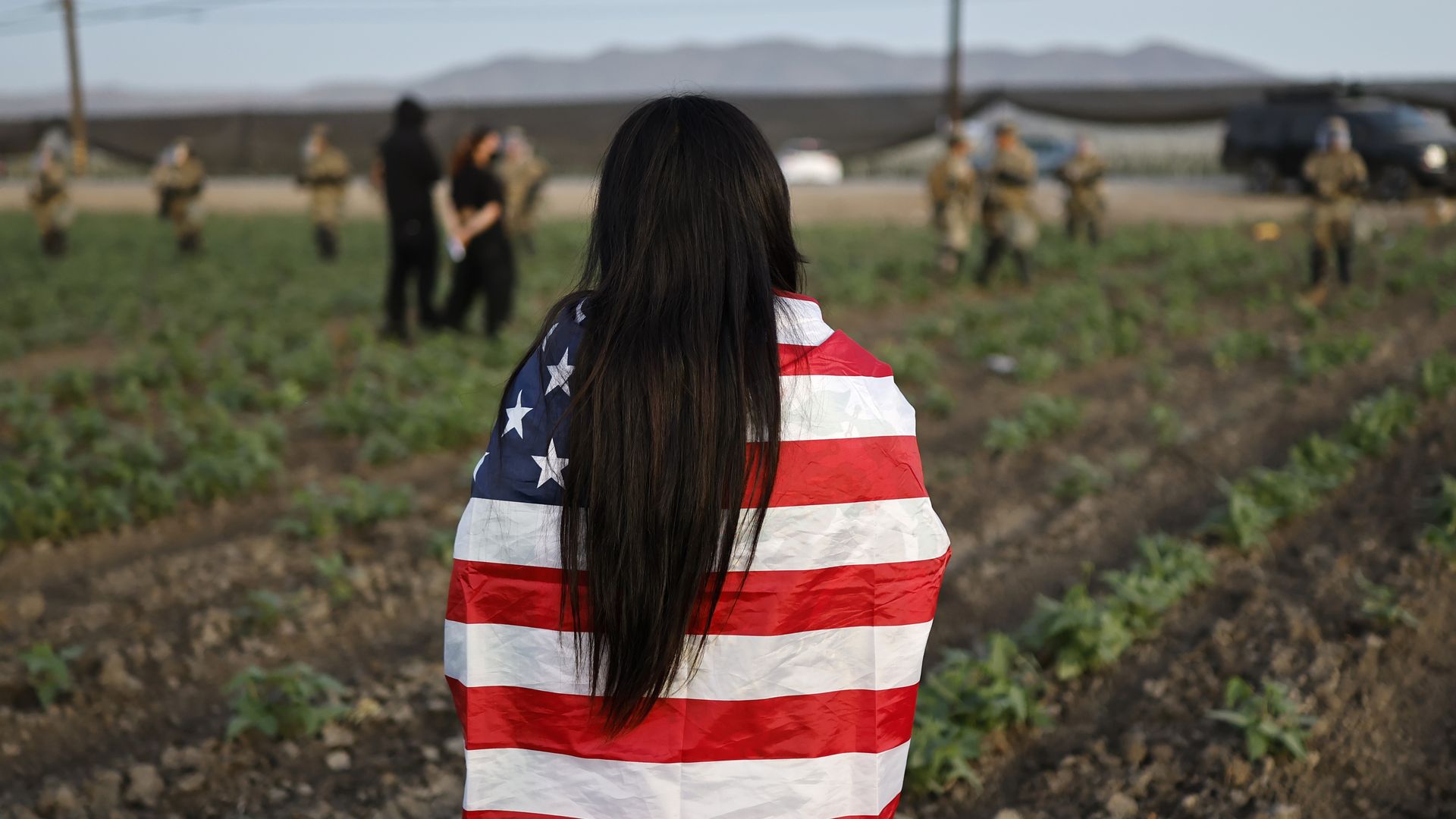 A demonstrator wears an American flag as National Guard soldiers block protestors during an ICE immigration raid at a nearby cannabis farm on July 10, 2025 near Camarillo, California.