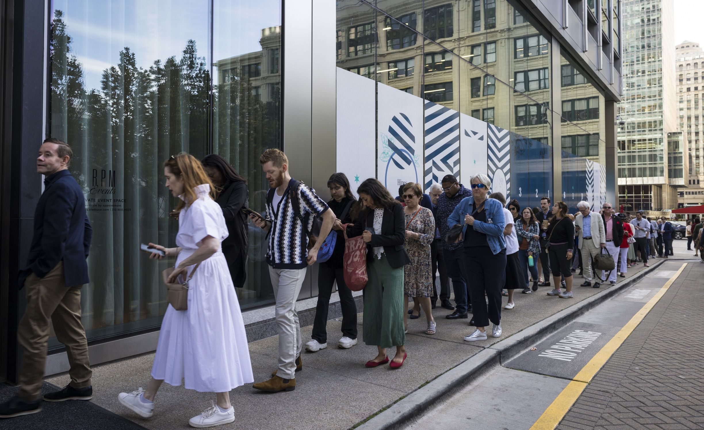 Long line of people waiting to get into a glass building.