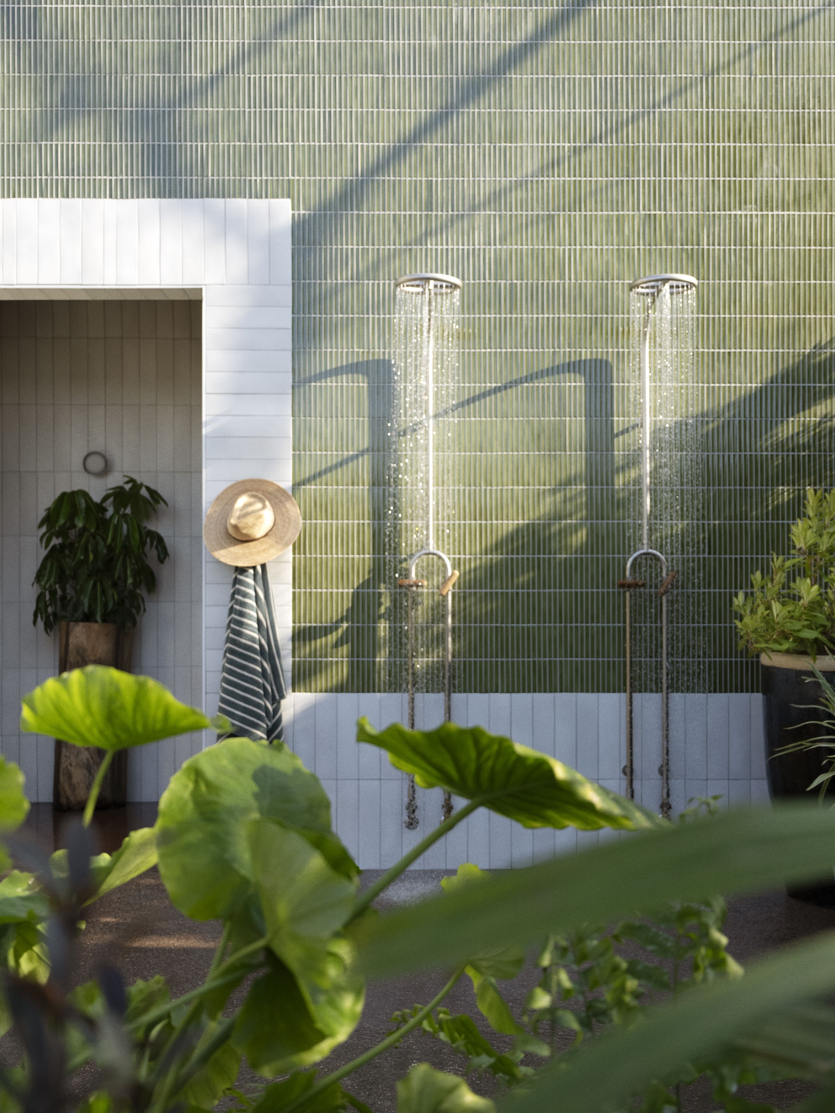 An outdoor shower area. Two showers are turned on and water pours below.
