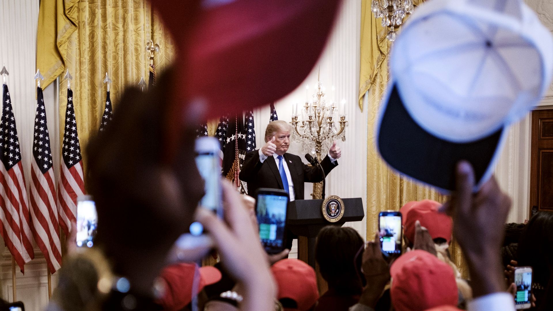 President Donald Trump gives two thumbs up to a crown of young black voters while they throw their MAGA hats in the air.