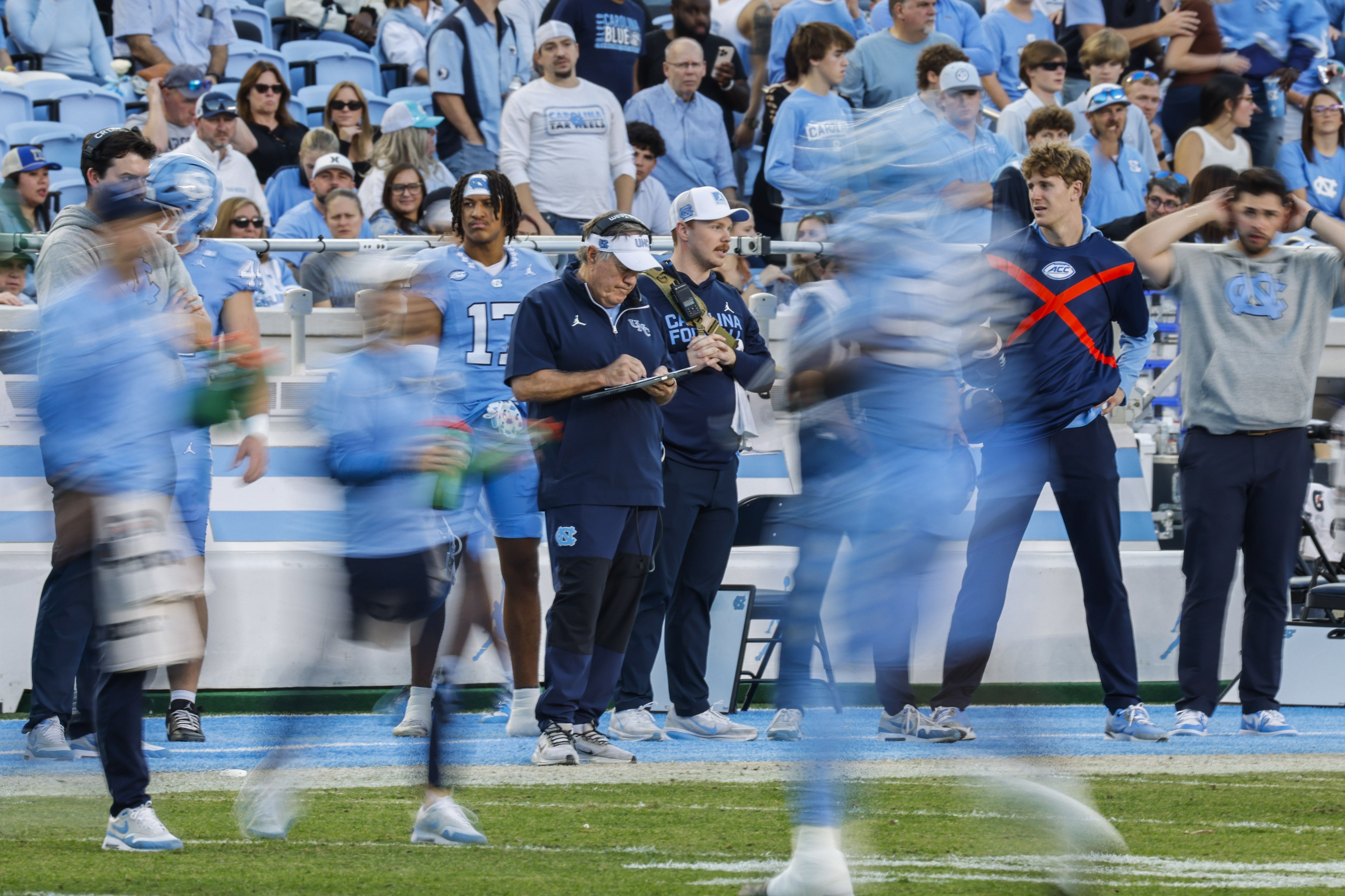Bill Belichick on the Tar Heels sideline during a loss to the Duke Blue Devils. Players are blurred in Carolina blue in the foreground.