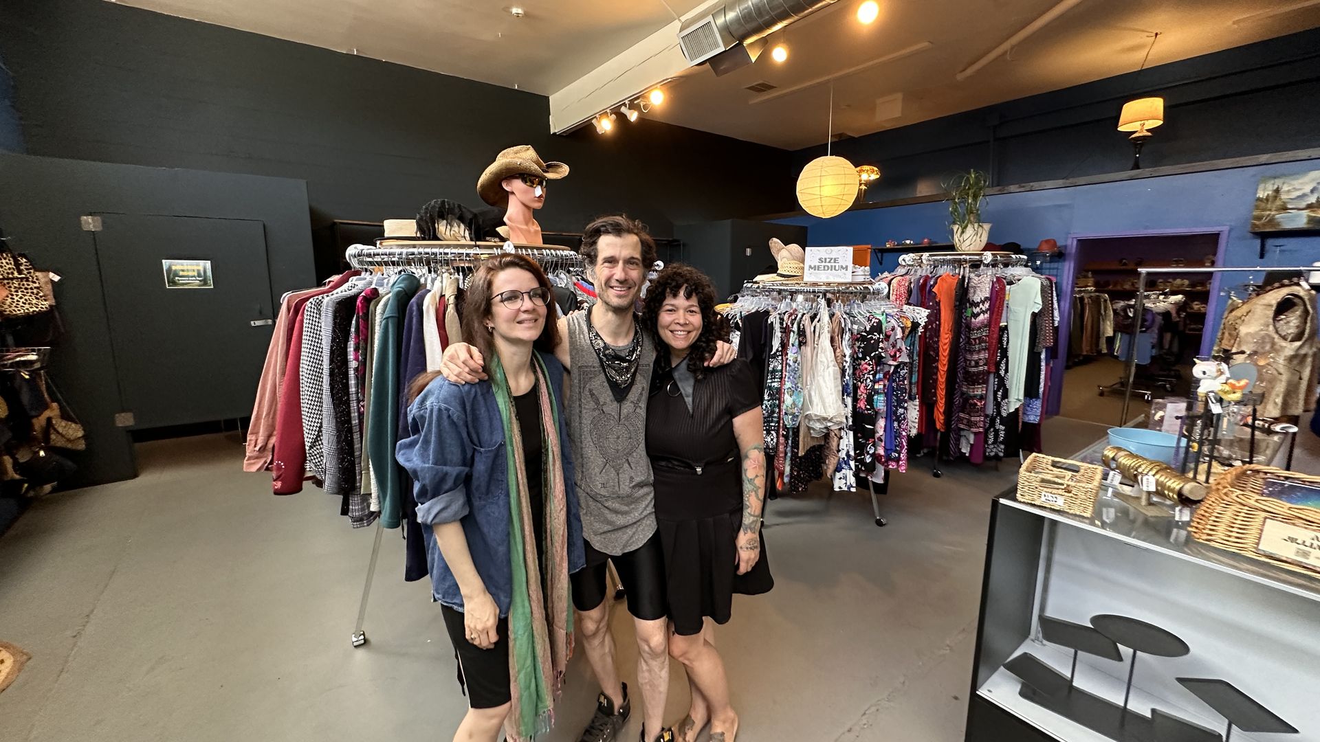 A man with his arms around the shoulder of a woman either side of him, in a thrift store