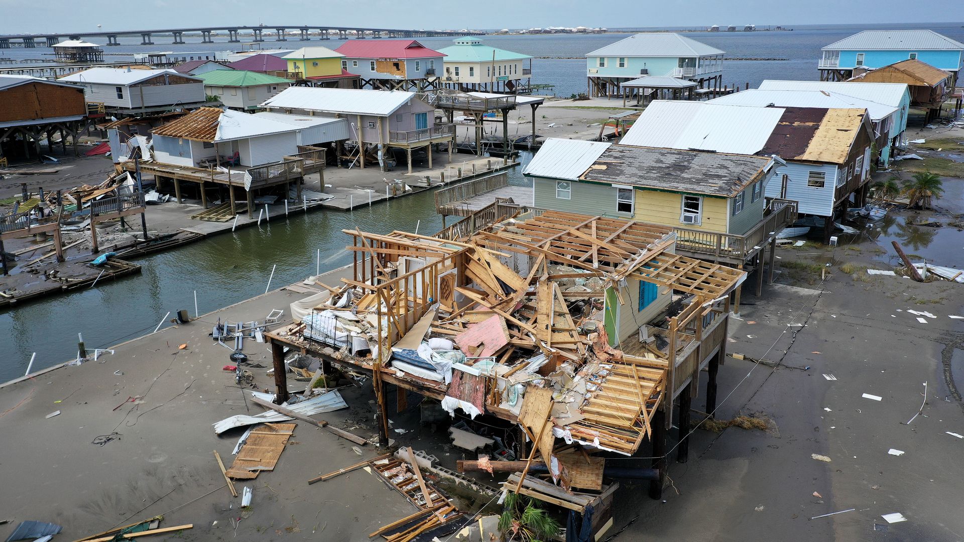 Homes on stilts at water's edge, house in foreground missing roof and outer walls.
