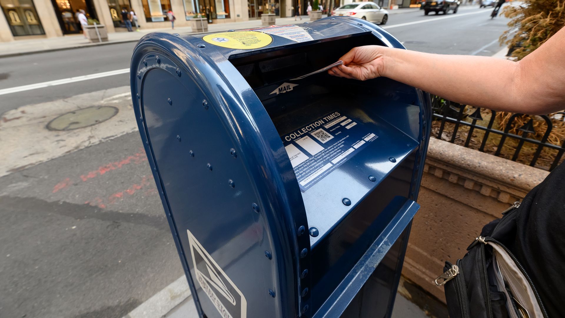 An arm puts a letter into a USPS mail box 