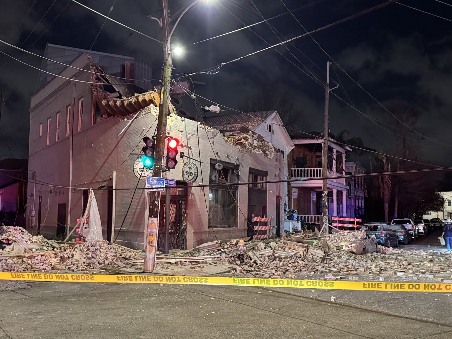 A partially collapsed brick building is photographed at night, with bricks spilling into both sides of a street corner.