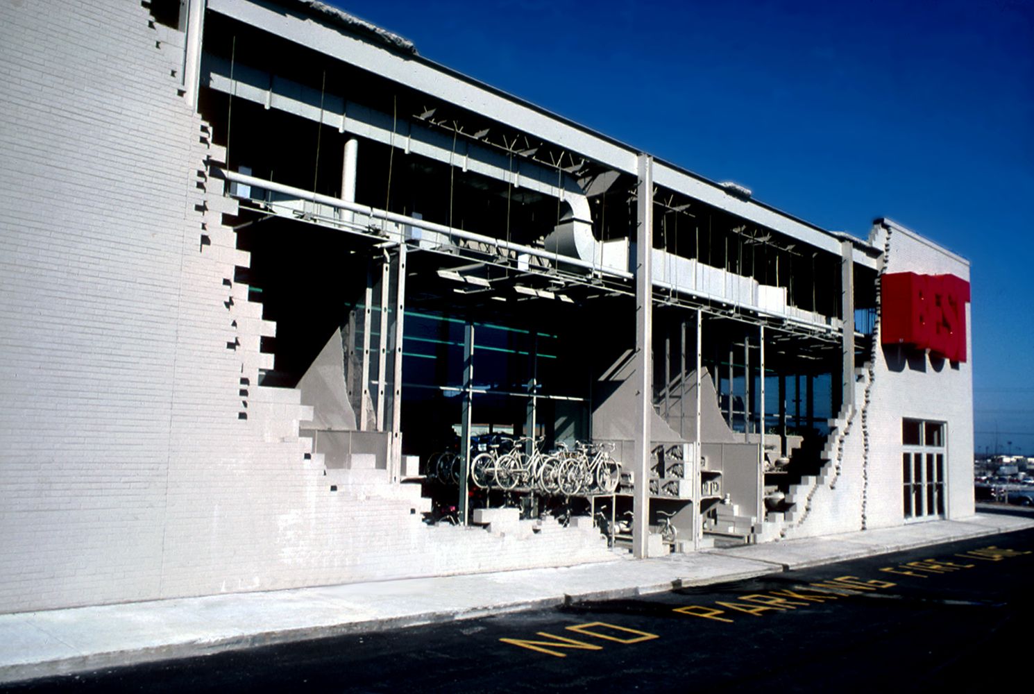 White modern building with exposed steel framework and an open storefront; bicycles parked near the front under a bright blue sky.