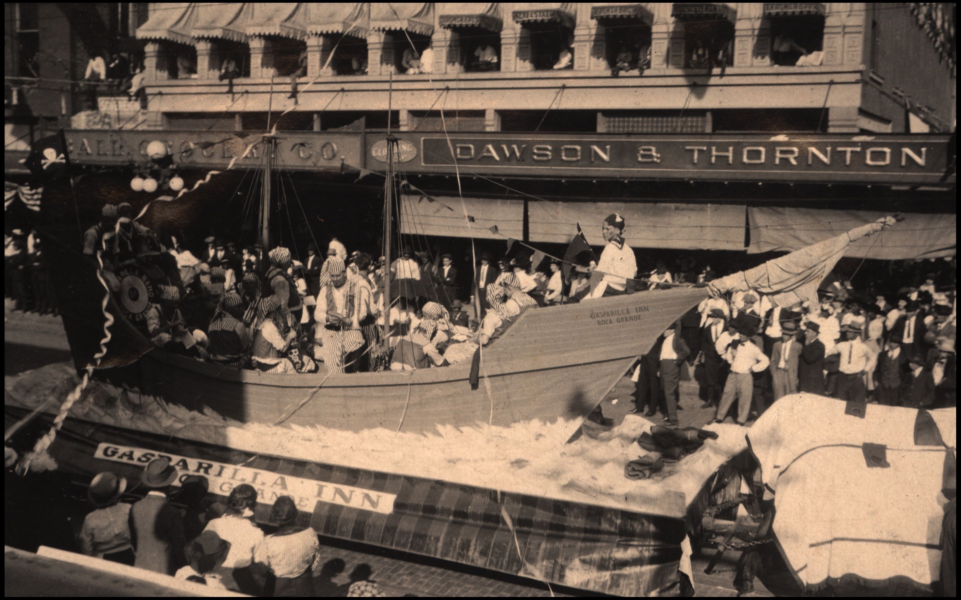 Black and white photo of a parade float shaped like a wooden ship labeled \