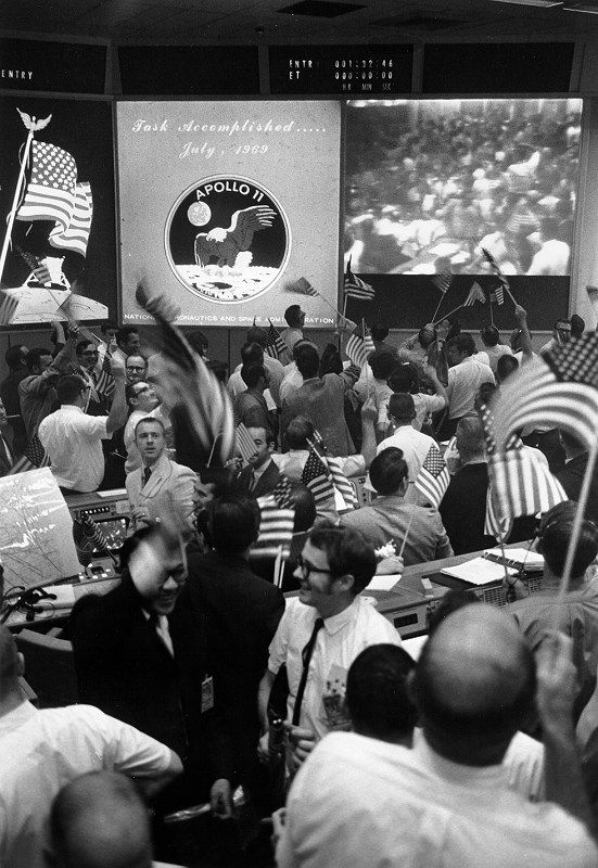 Black and white photo of people celebrating with small American flags. 