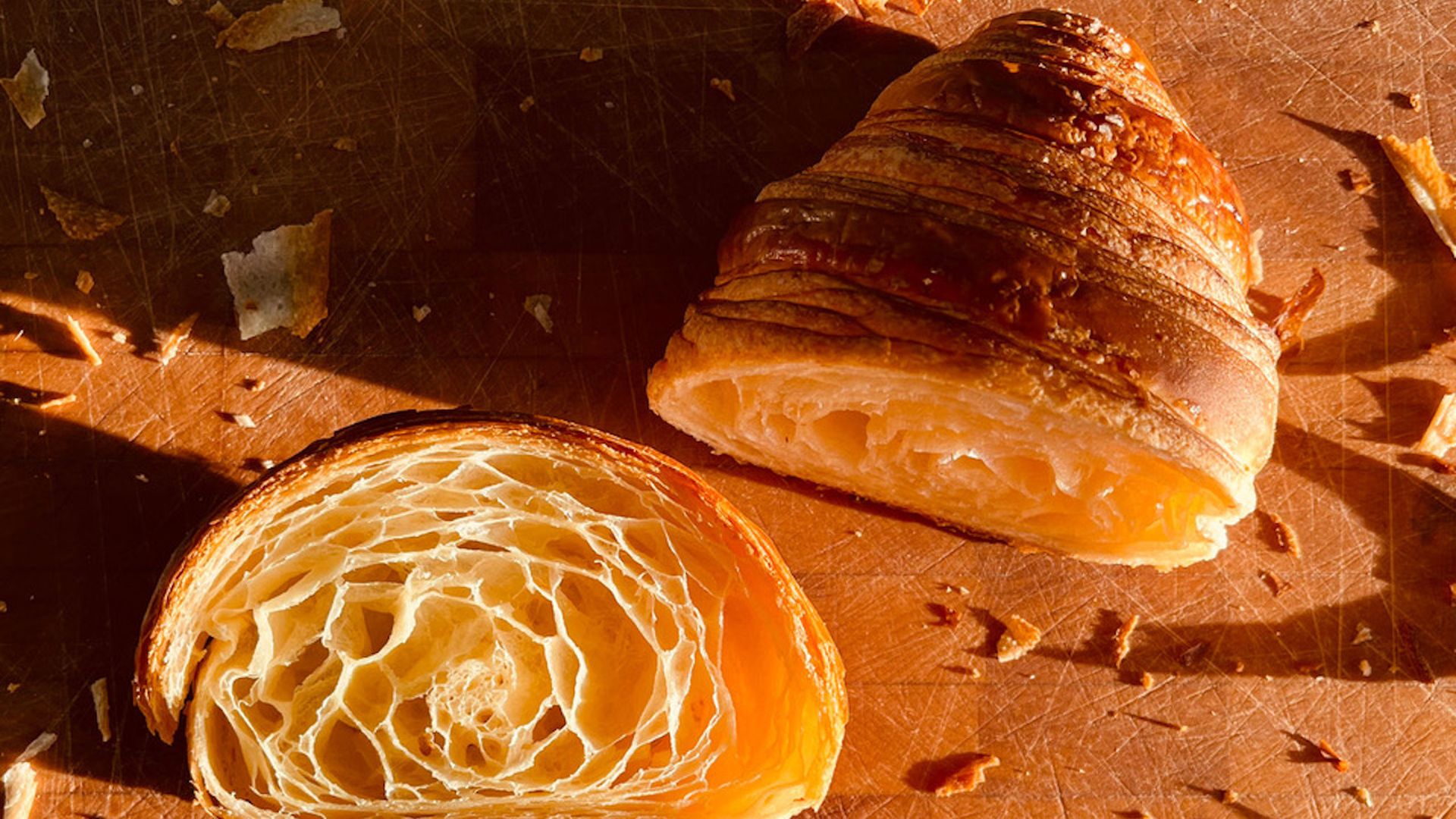 A golden croissant cut in half with crumbs on a cutting board.