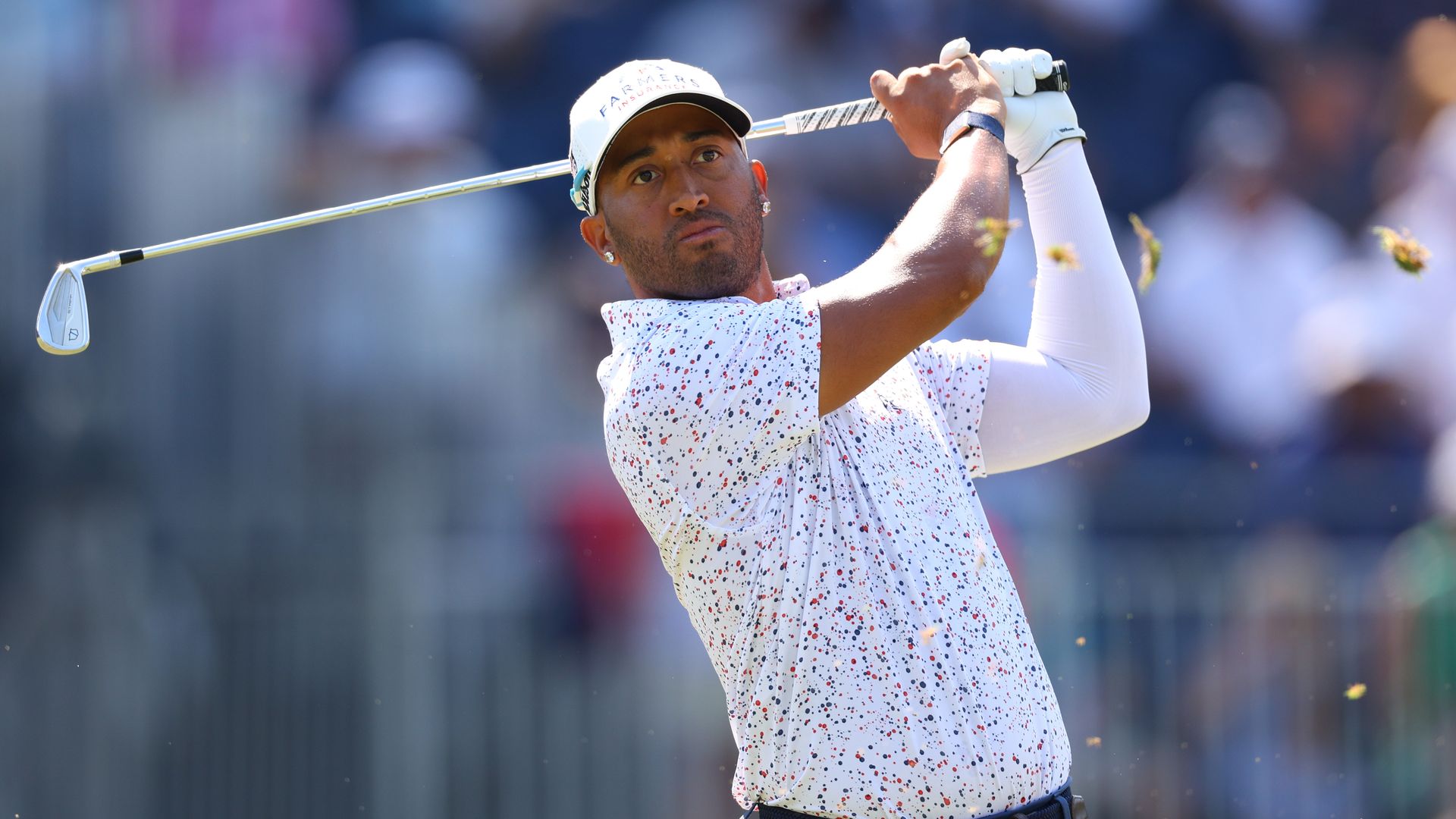 Mack is shown just having hit the ball, watching where it goes. He's wearing a patterned polo and hat.