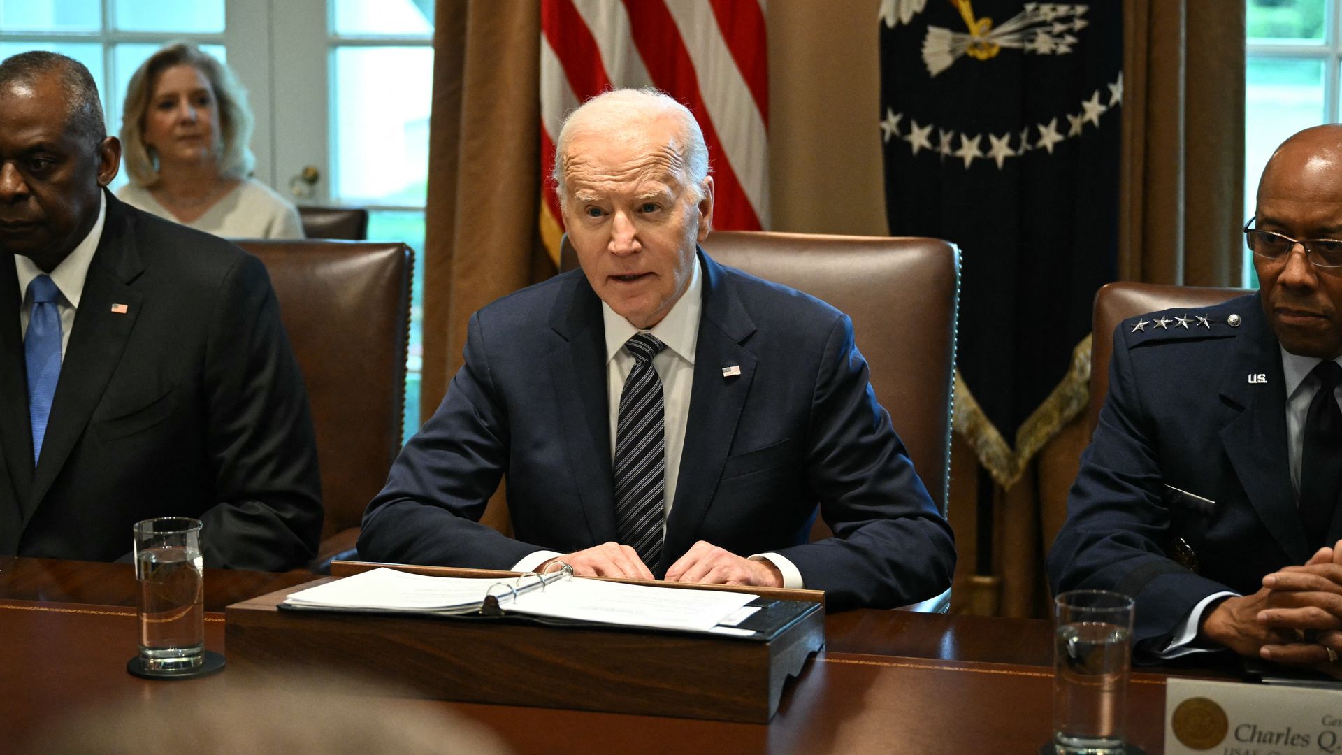 President Biden, wearing a blue suit, white shirt and blue and white striped tie, speaking at a table flanked by Pentagon officials.