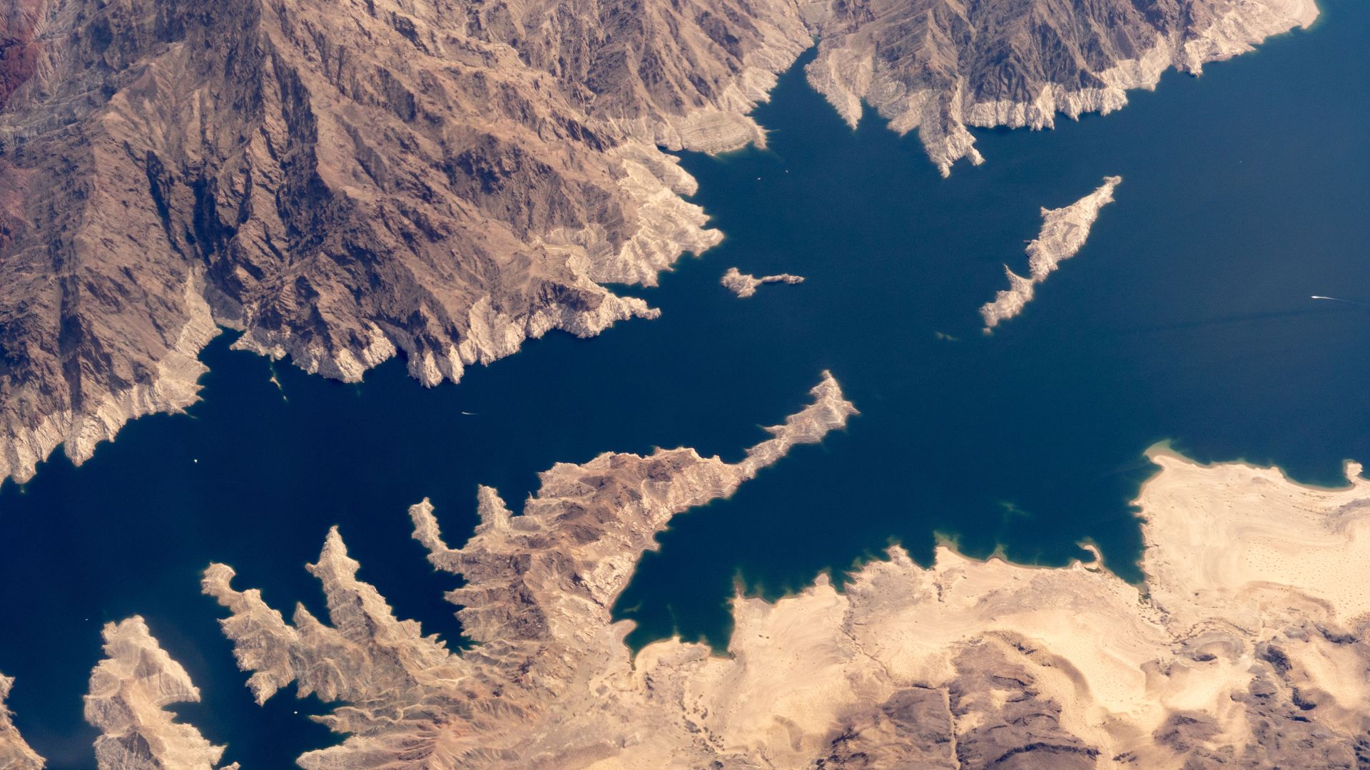 Aerial view of a lake with a jagged shoreline, with a white ring around shore indicating a reduction in water levels. 