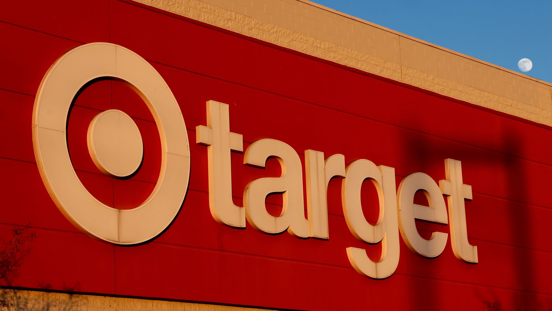 Red and beige Target store sign on building exterior with a clear blue sky and visible moon in the background.