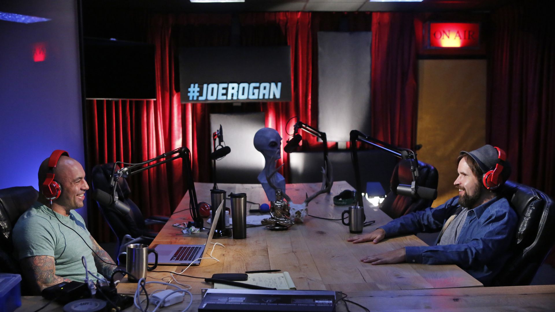 Two men with headphones sitting across from each other at mics