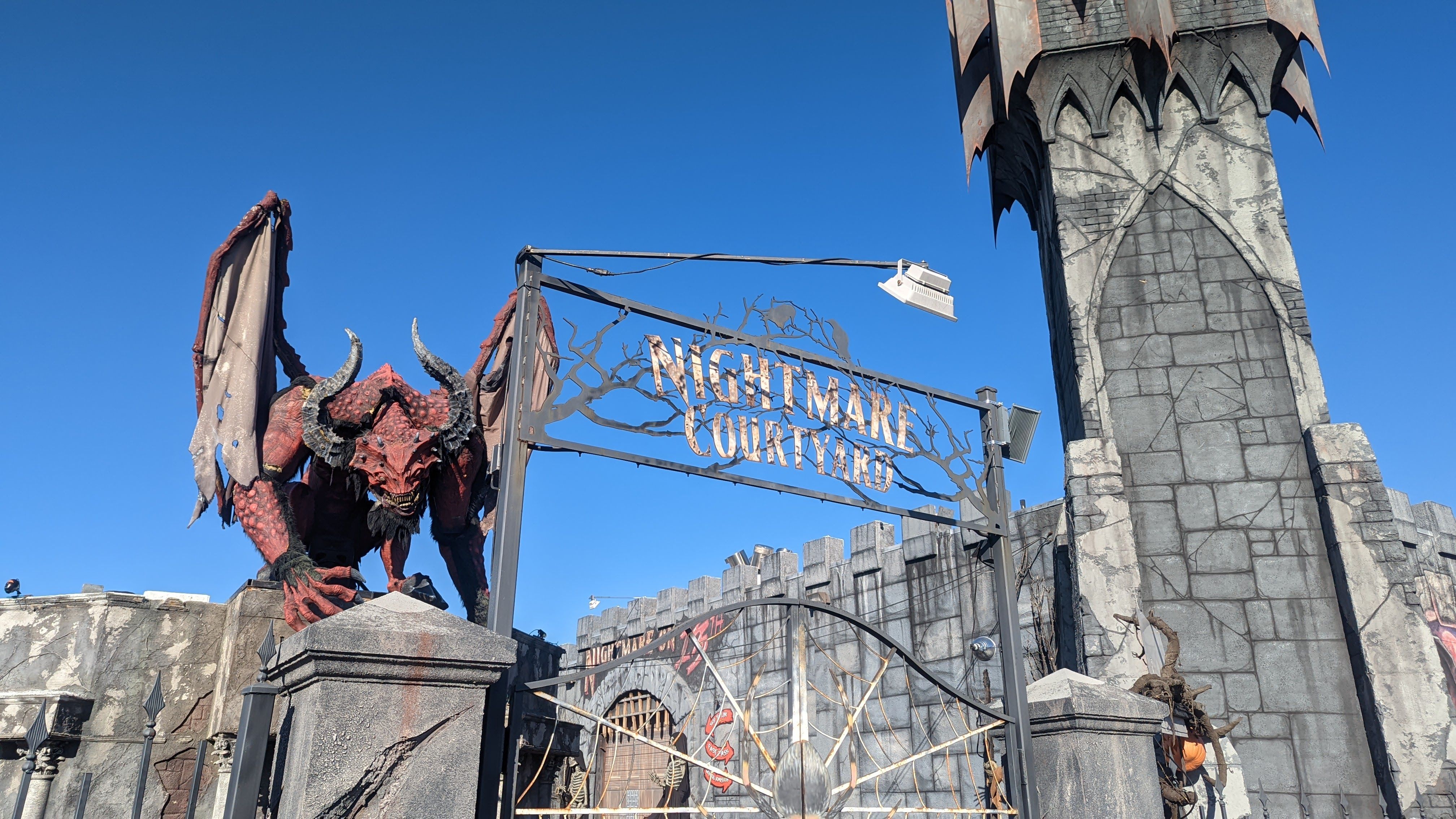 A winged demon animatronic stands next to a jagged castle tower and a sign that reads "Nightmare Courtyard."