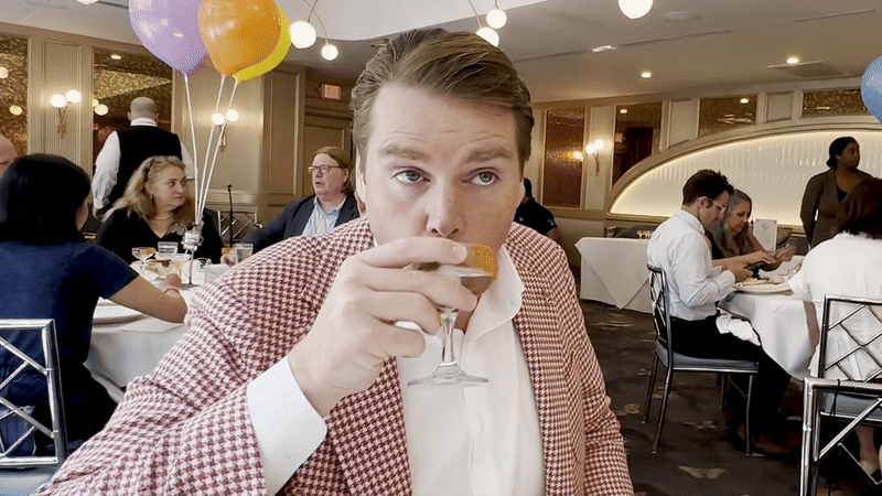 A man in a red houndstooth jacket drinks a martini.