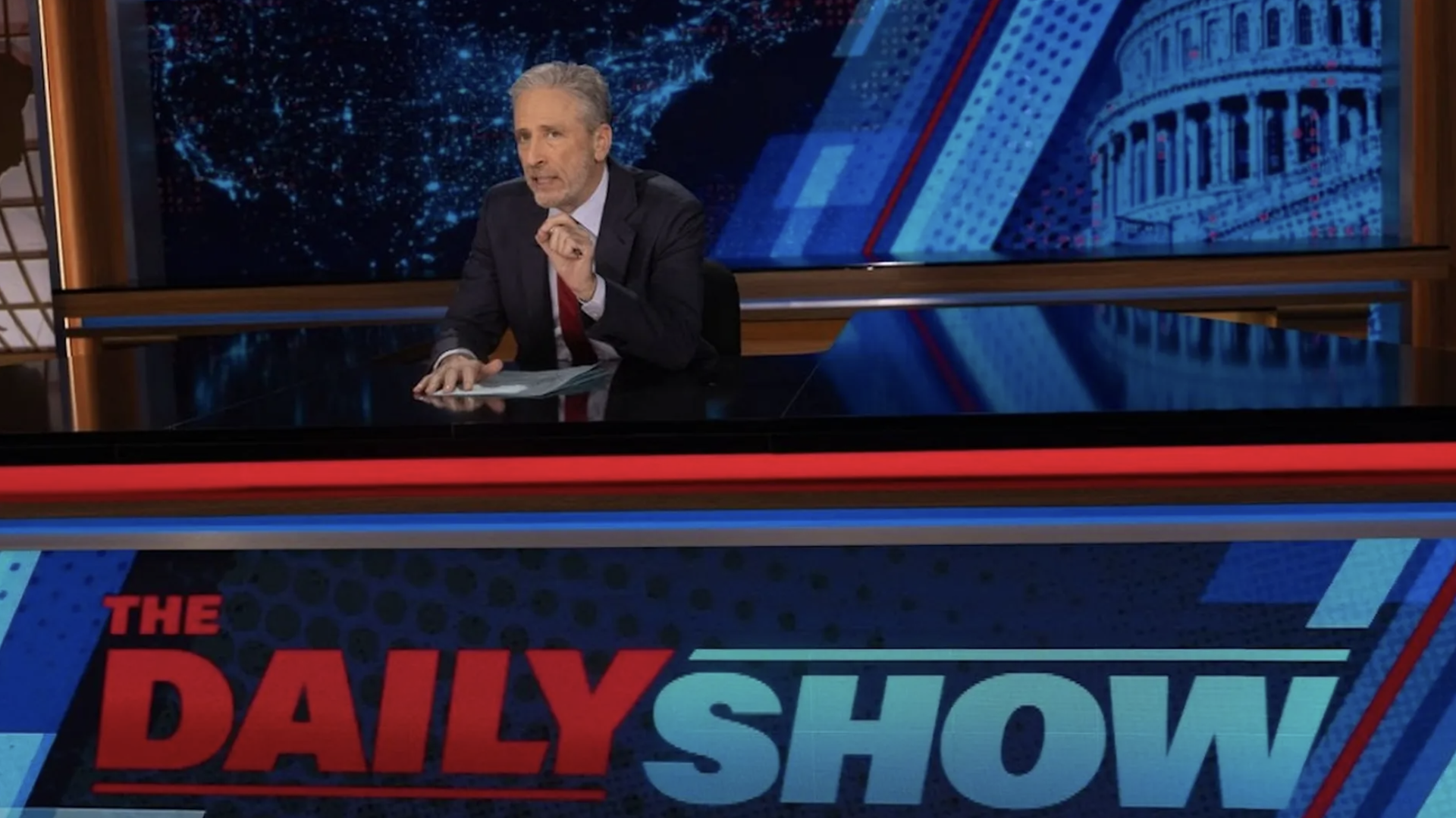Jon Stewart sitting behind the Daily Show desk