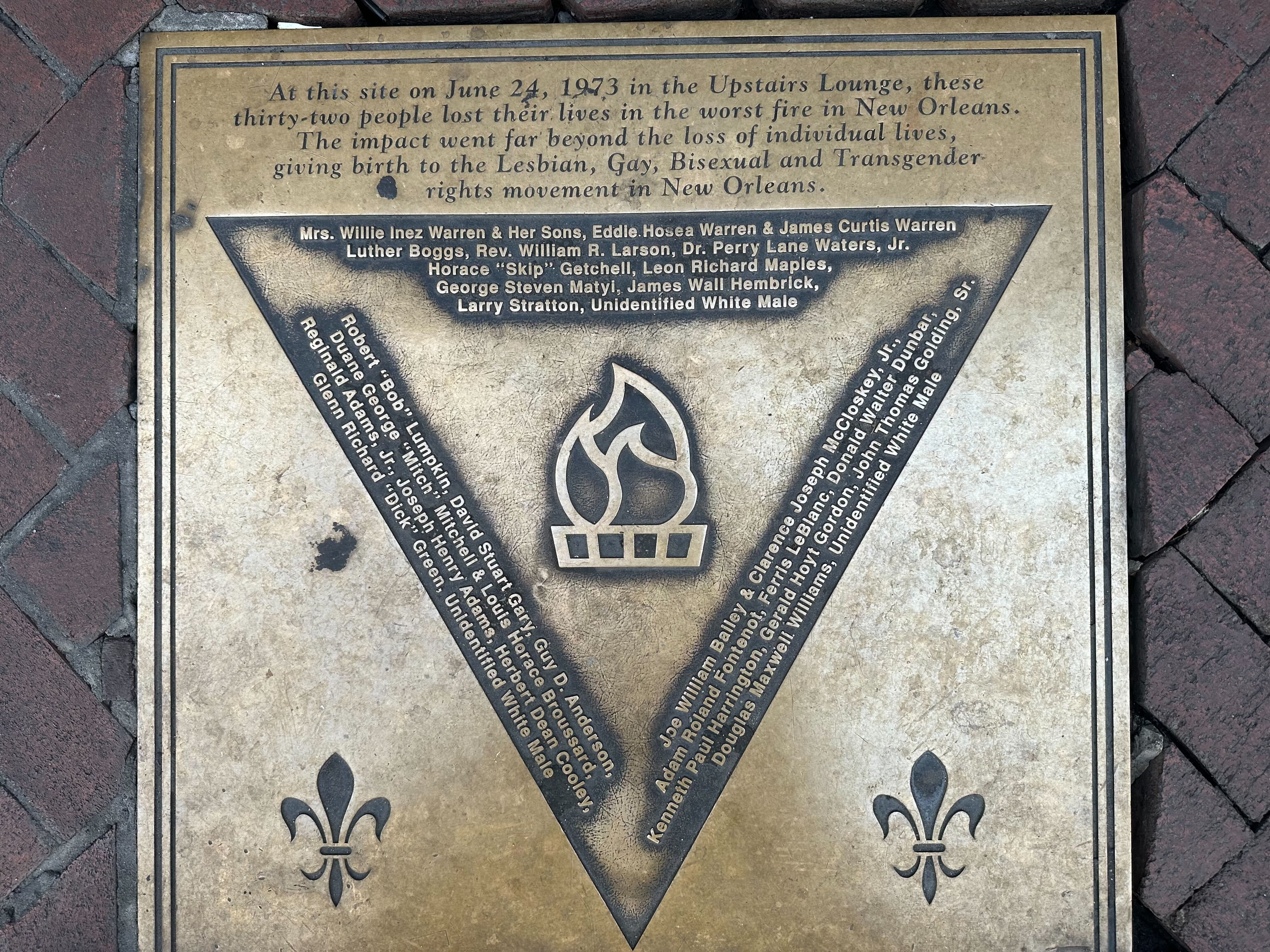 Image shows a memorial plaque for the UpStairs Lounge fire with the names of the 32 victims.