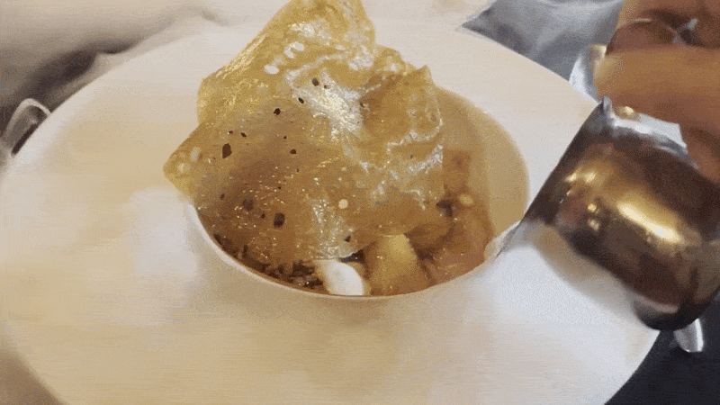 A moving image of a cloud of dry ice vapor escaping around a small dish with a golden dessert.
