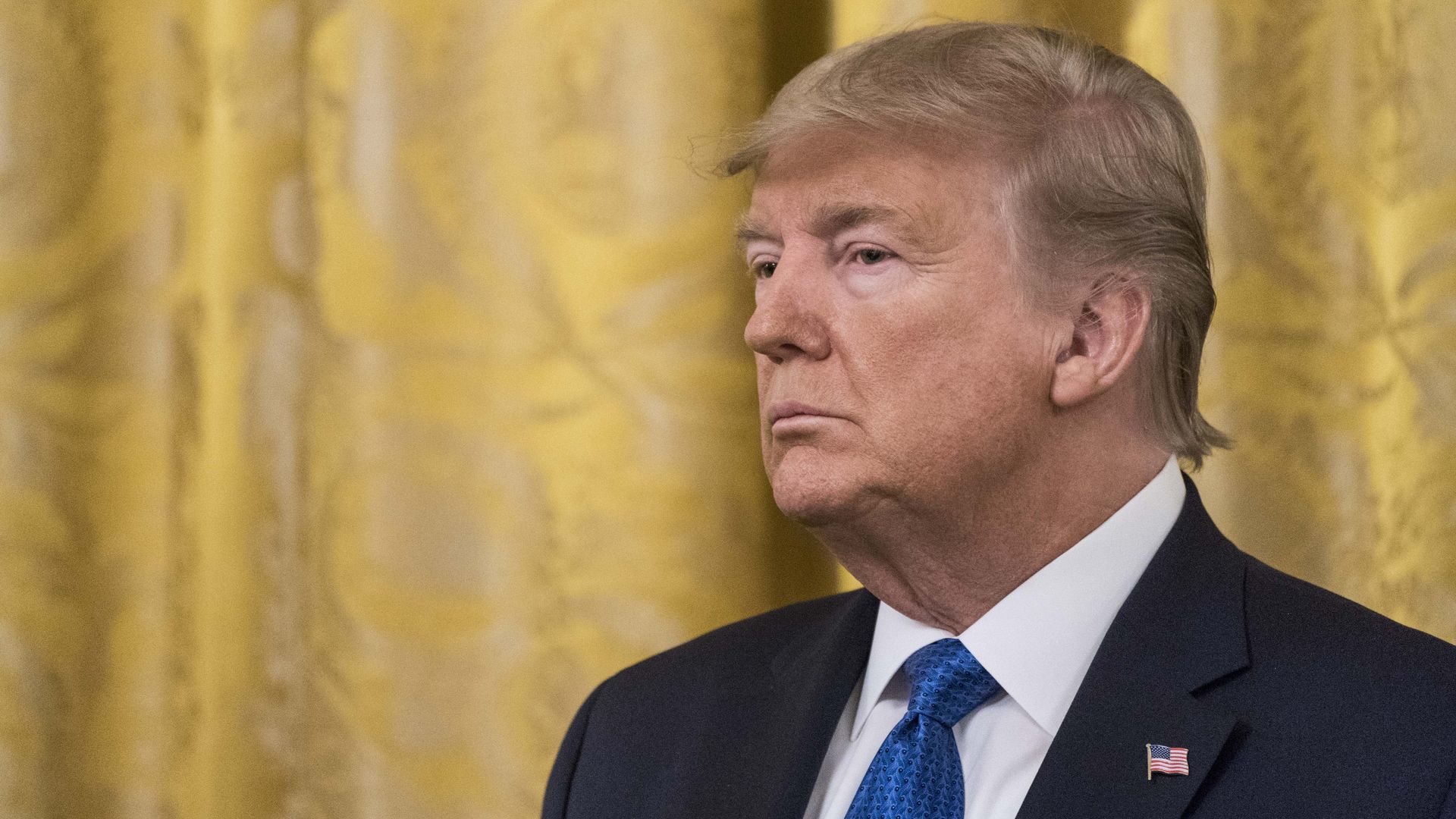 In this image, President Trump stands in a suit and tie.