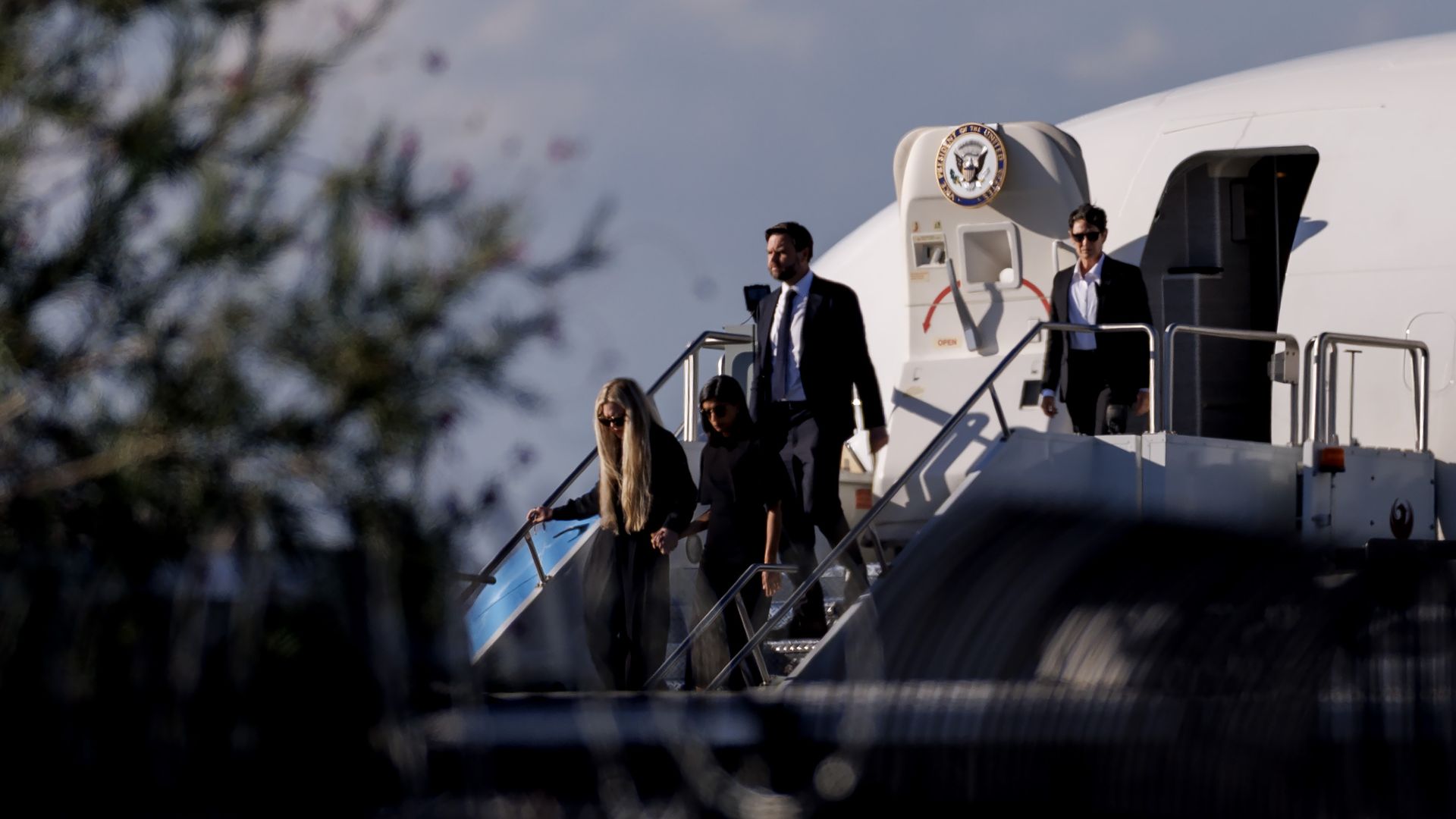 JD Vance descends the stairs out of Air Force Two with his wife and Erika Kirk, who are wearing black and holding hands.