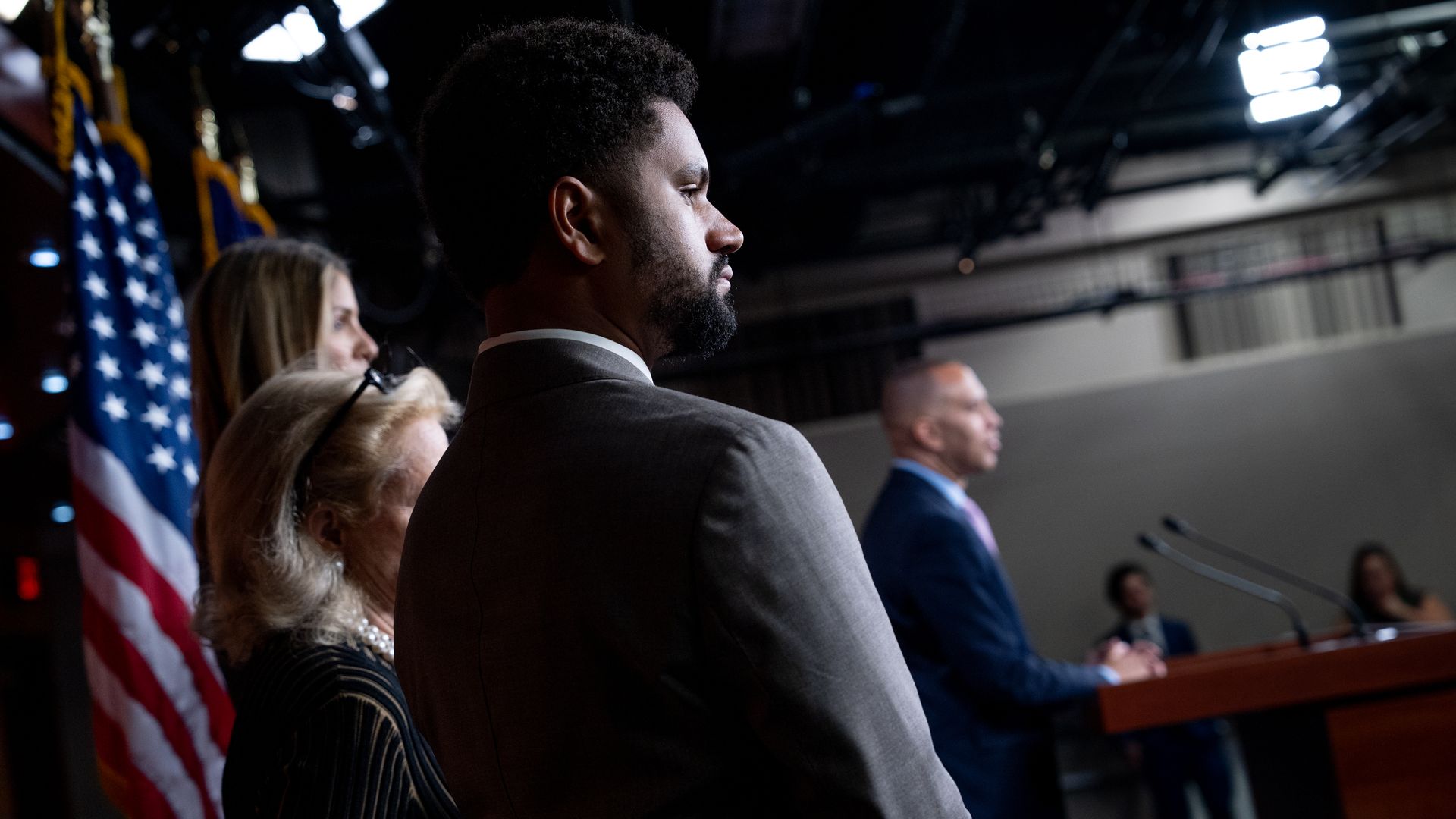 Rep. Maxwell Frost, wearing a gray suit and standing next to American flags.