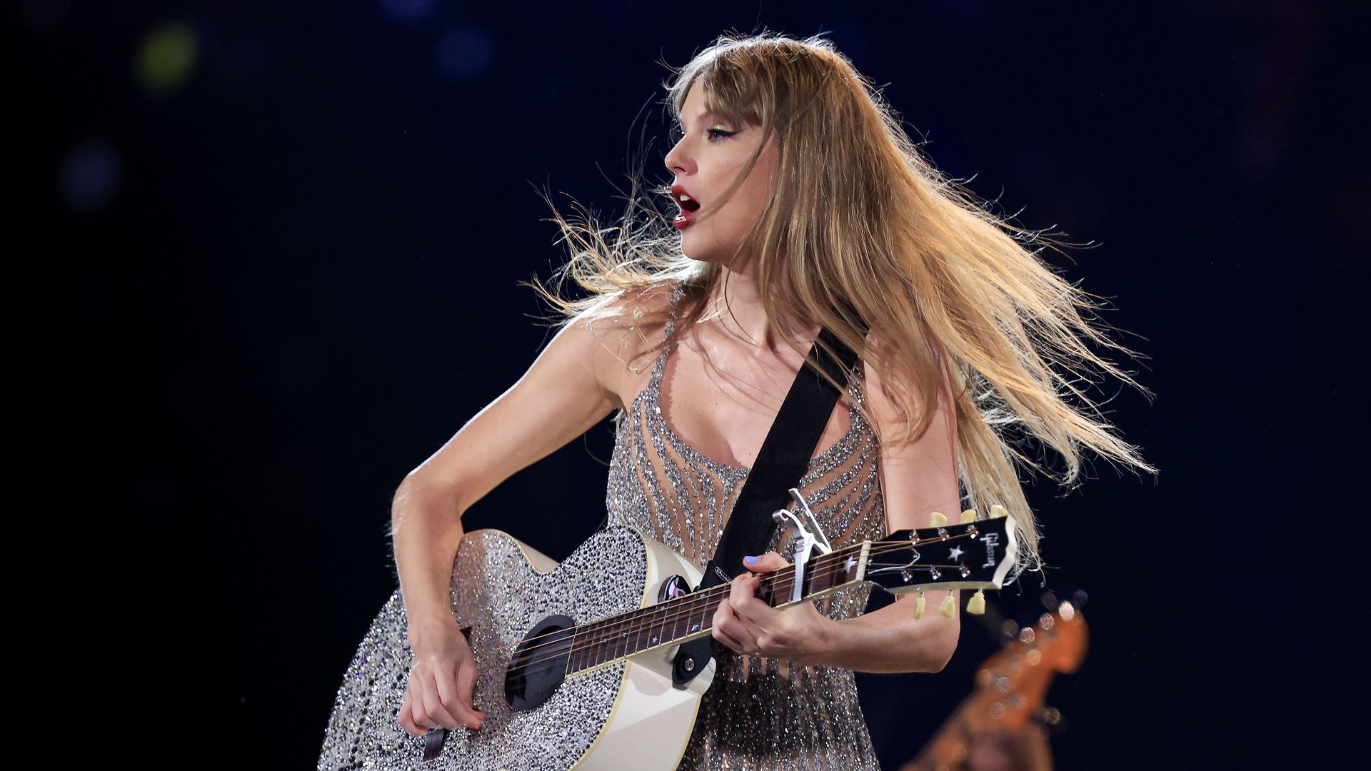 Taylor Swift strumming a guitar on stage.
