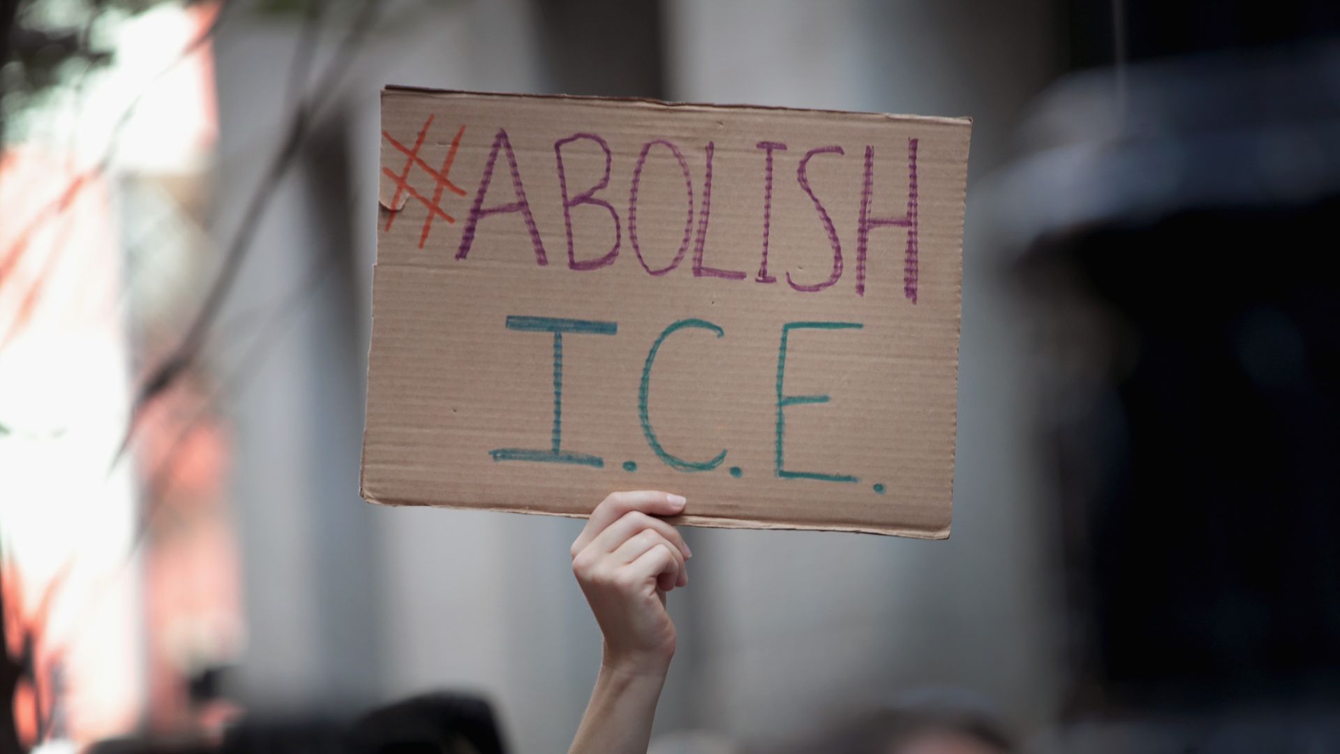 A hand holding up a cardboard sign that has "Abolish ICE" written on it