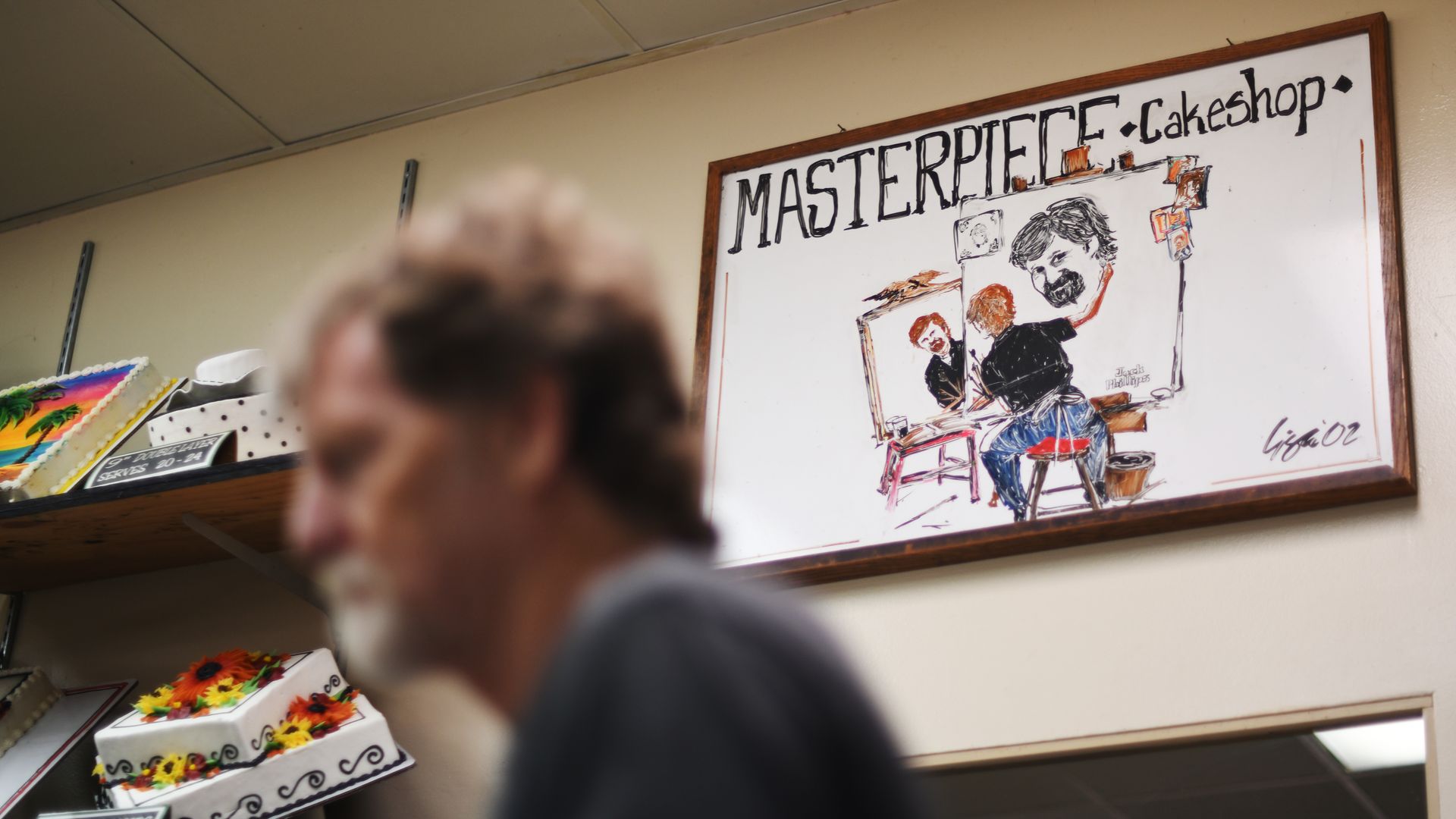 Photo of a cake shop with an art piece that says "Masterpiece Cakeshop" and an illustration of owner Jack Phillips