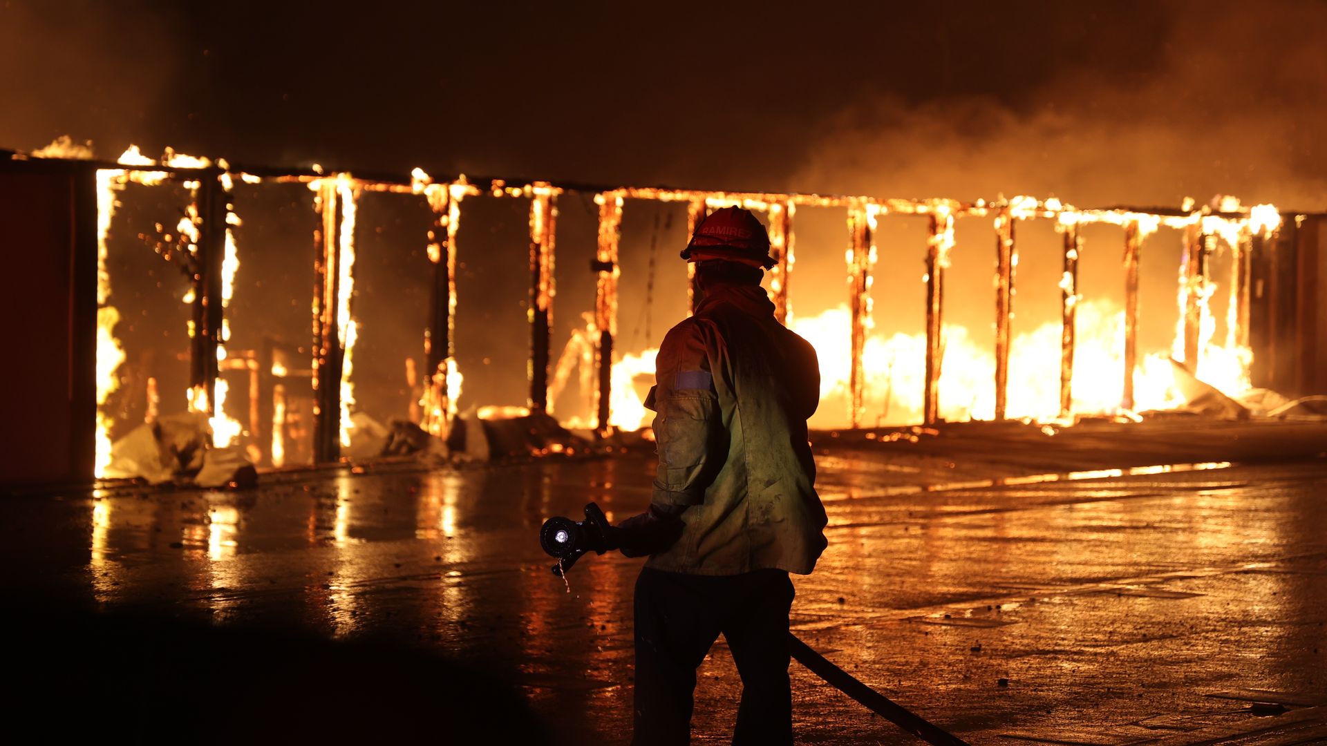 A firefighter stands in front of a hollowed out structure that's still on fire