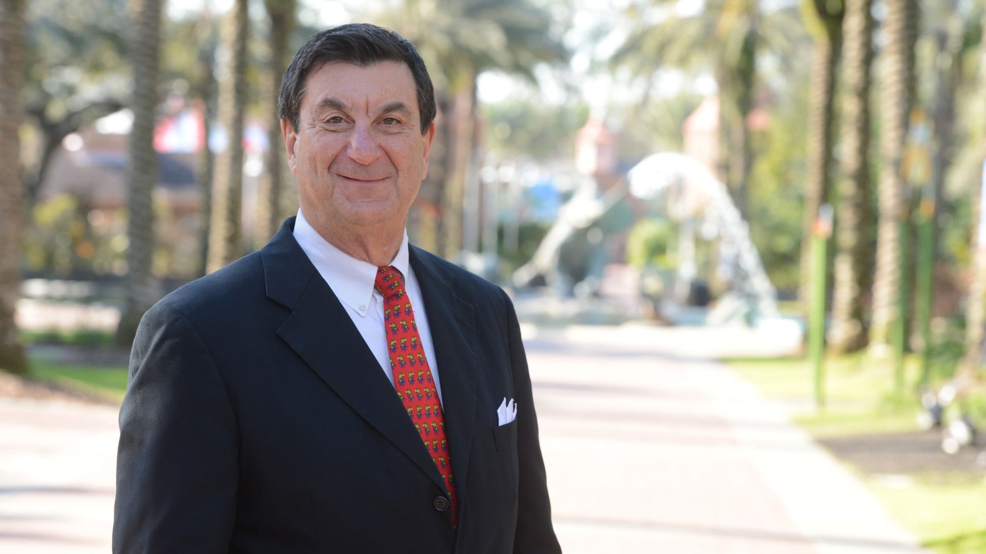 Photo shows Ron Forman in a suit standing in front of the elephant fountain at Audubon Zoo in New Orleans