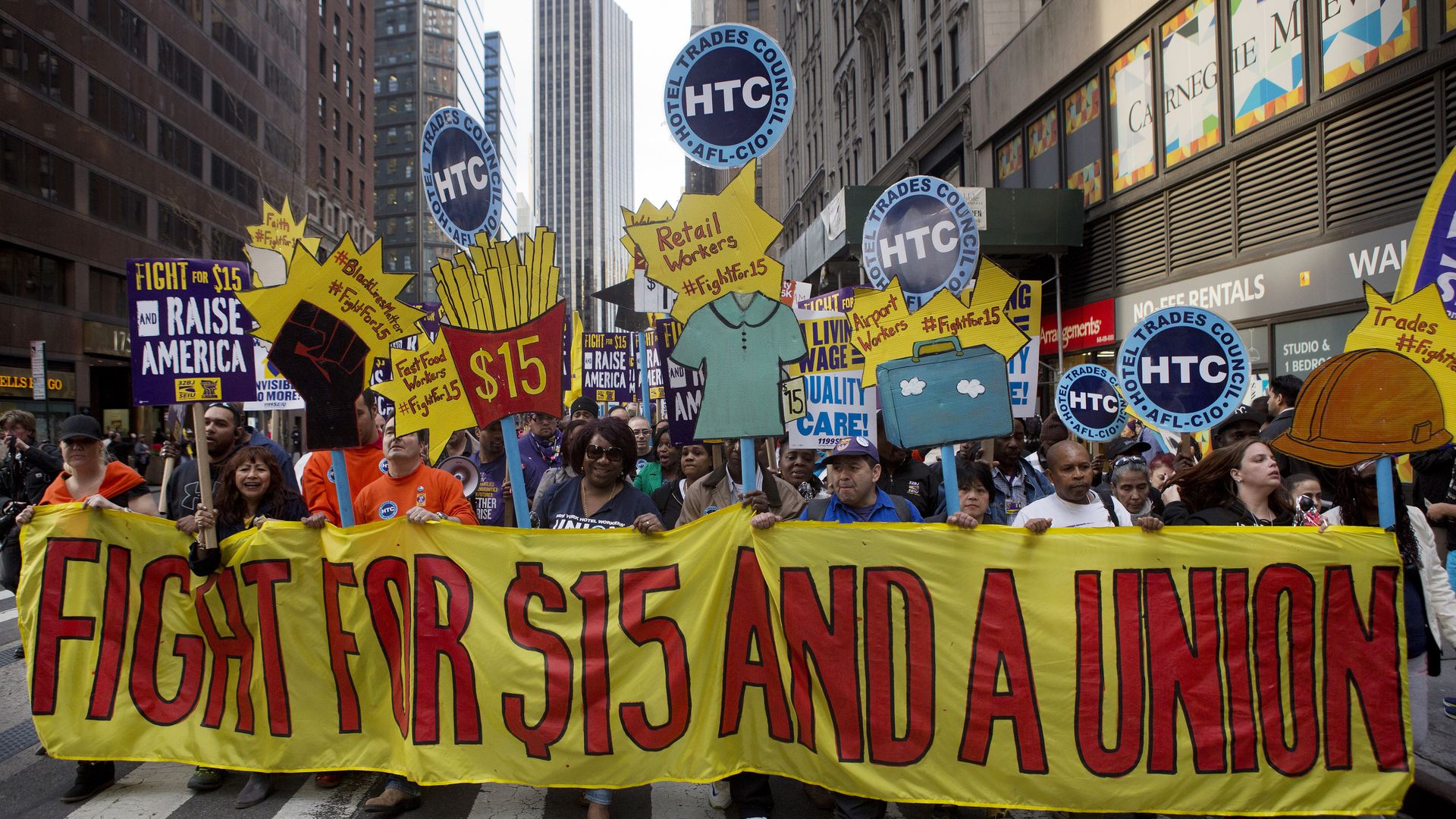 Picture of a protest where people are holding a yellow banner that says "FIGHT FOR $15 AND A UNION"