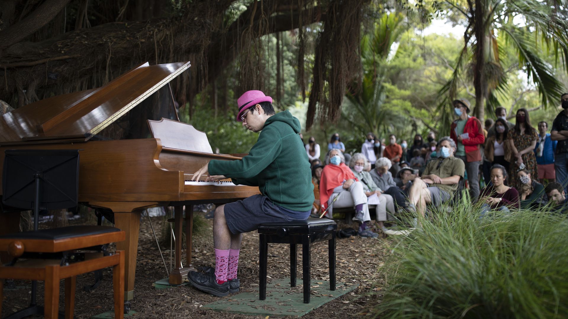Photo of a person playing the piano in a park setting with spectators
