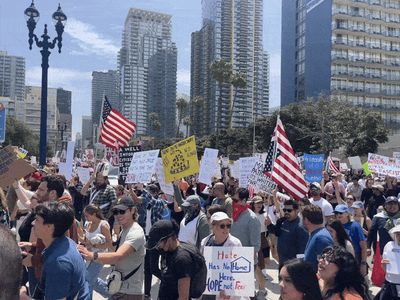 A large group of protesters march through downtown San Diego with signs and flags during a "No Kings" rally. 