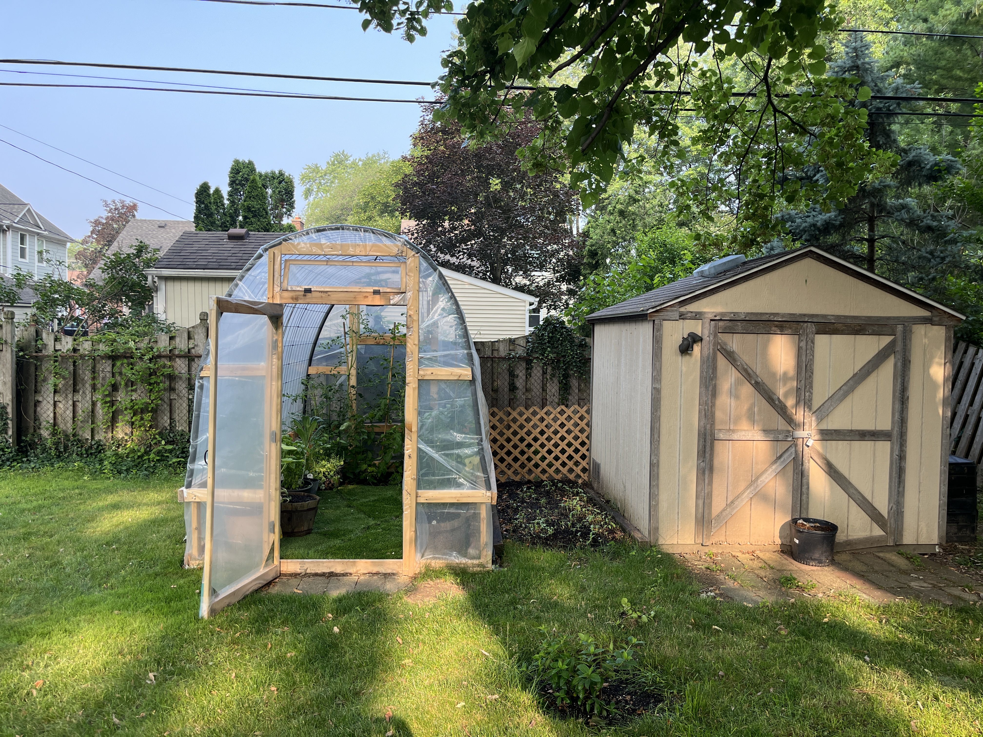 A greenhouse next to a shed with a patch of dirt in the middle